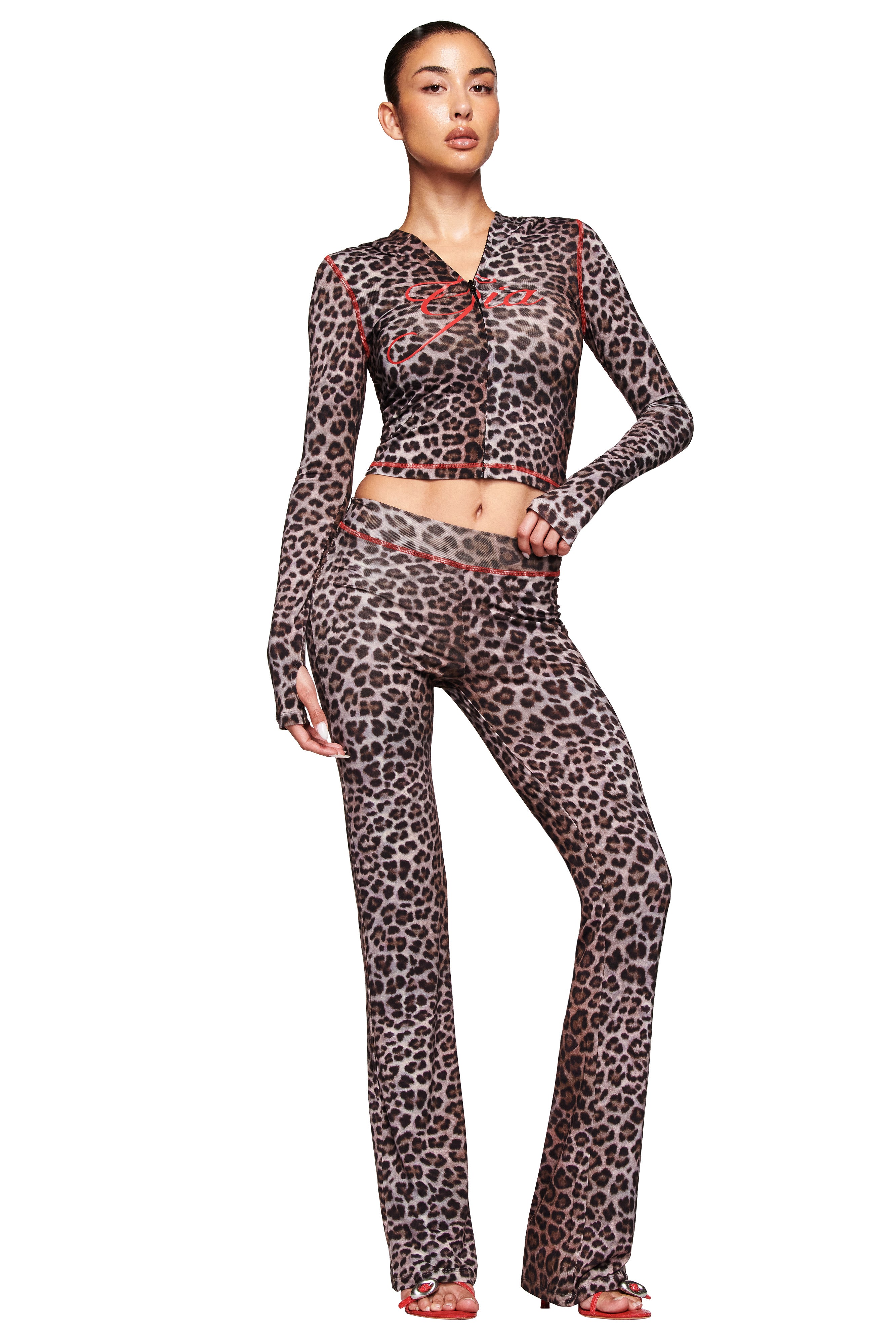A woman poses confidently with one hand on her hip, wearing the I.AM.GIA BLARE TRACKPANT in Dark Leopard and a matching crop top with red accents, set against a white background.