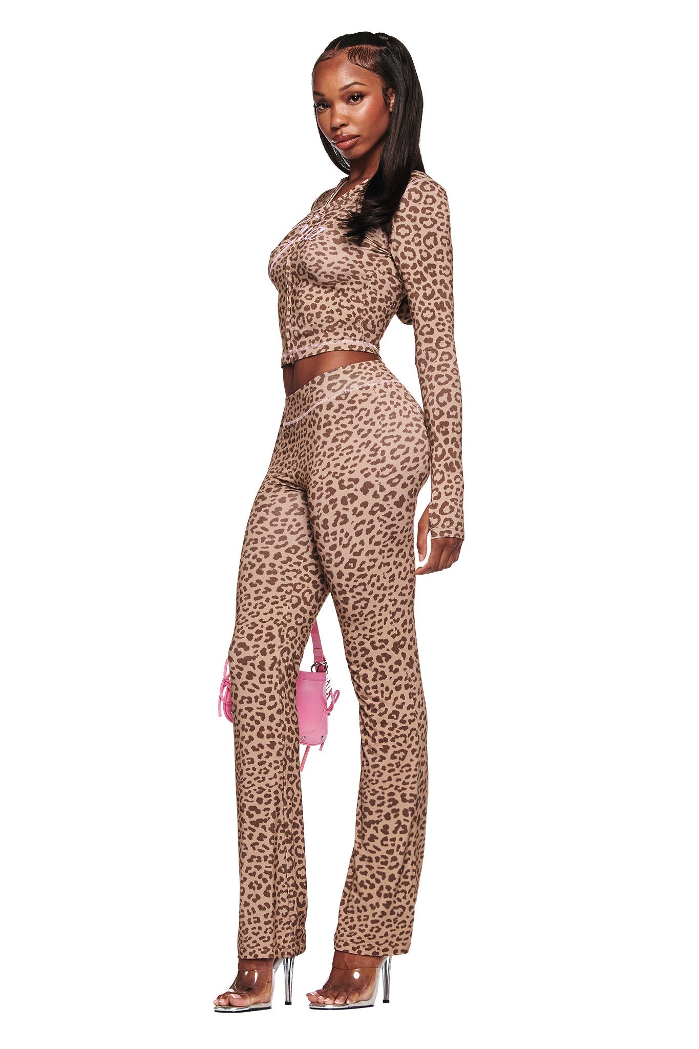 A woman in profile wears the I.AM.GIA BLARE HOODIE in mocha leopard print with matching pants, accessorized with a small pink bag and clear high-heeled sandals, posed against a white background.
