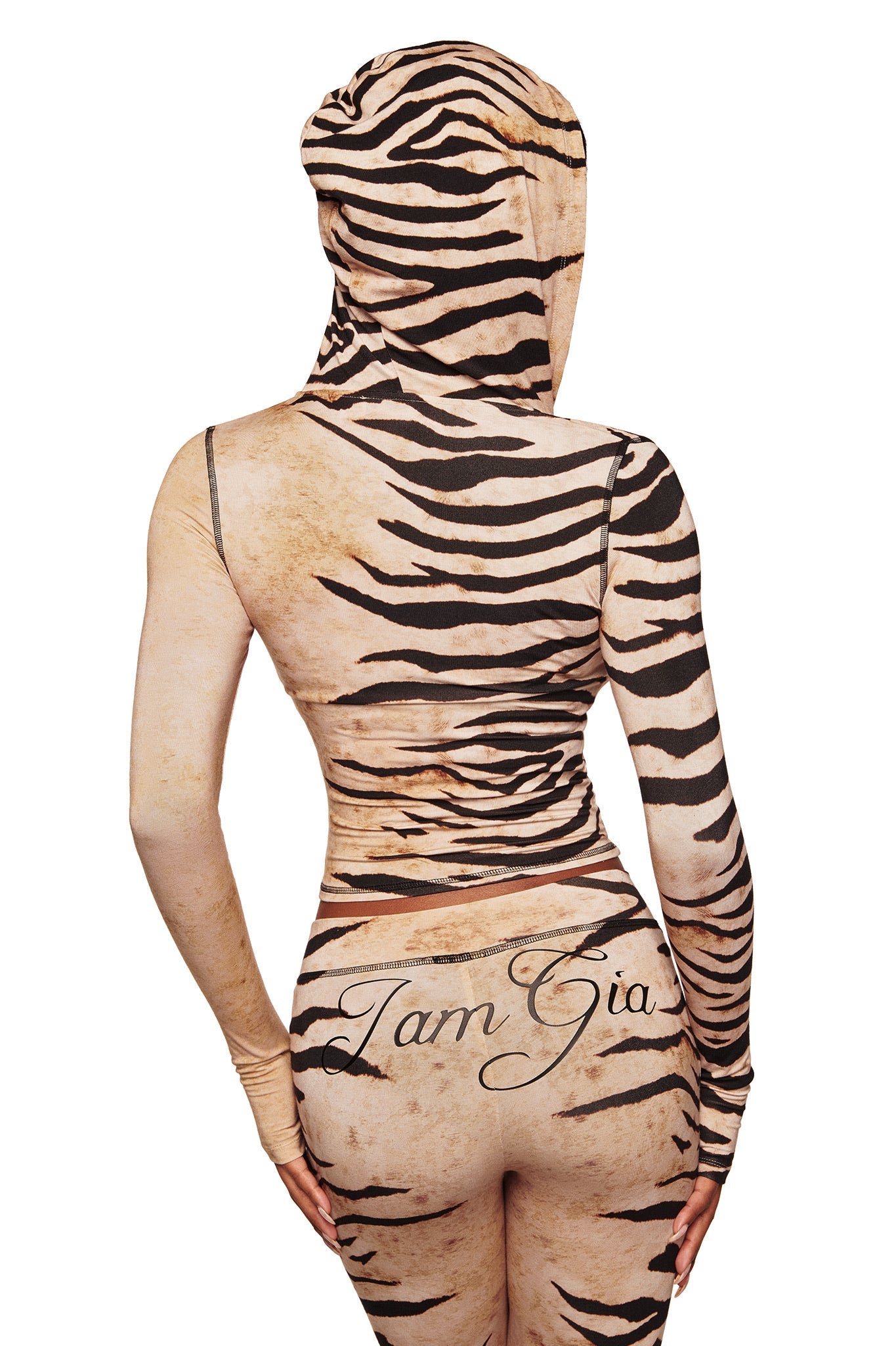 A person in the I.AM.GIA BLARE HOODIE - WILD SIDE, a hooded, long-sleeve, tiger-striped bodysuit with “I.AM.GIA” on the back, is seen from behind against a white background.