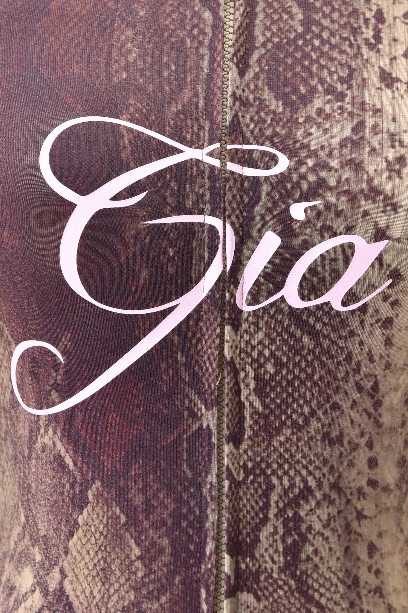 Close-up of the BLARE HOODIE - SNAKE by I.AM.GIA, featuring a brown snake print and "Gia" in large, elegant light pink script across the fabric. A vertical seam is visible down the center.