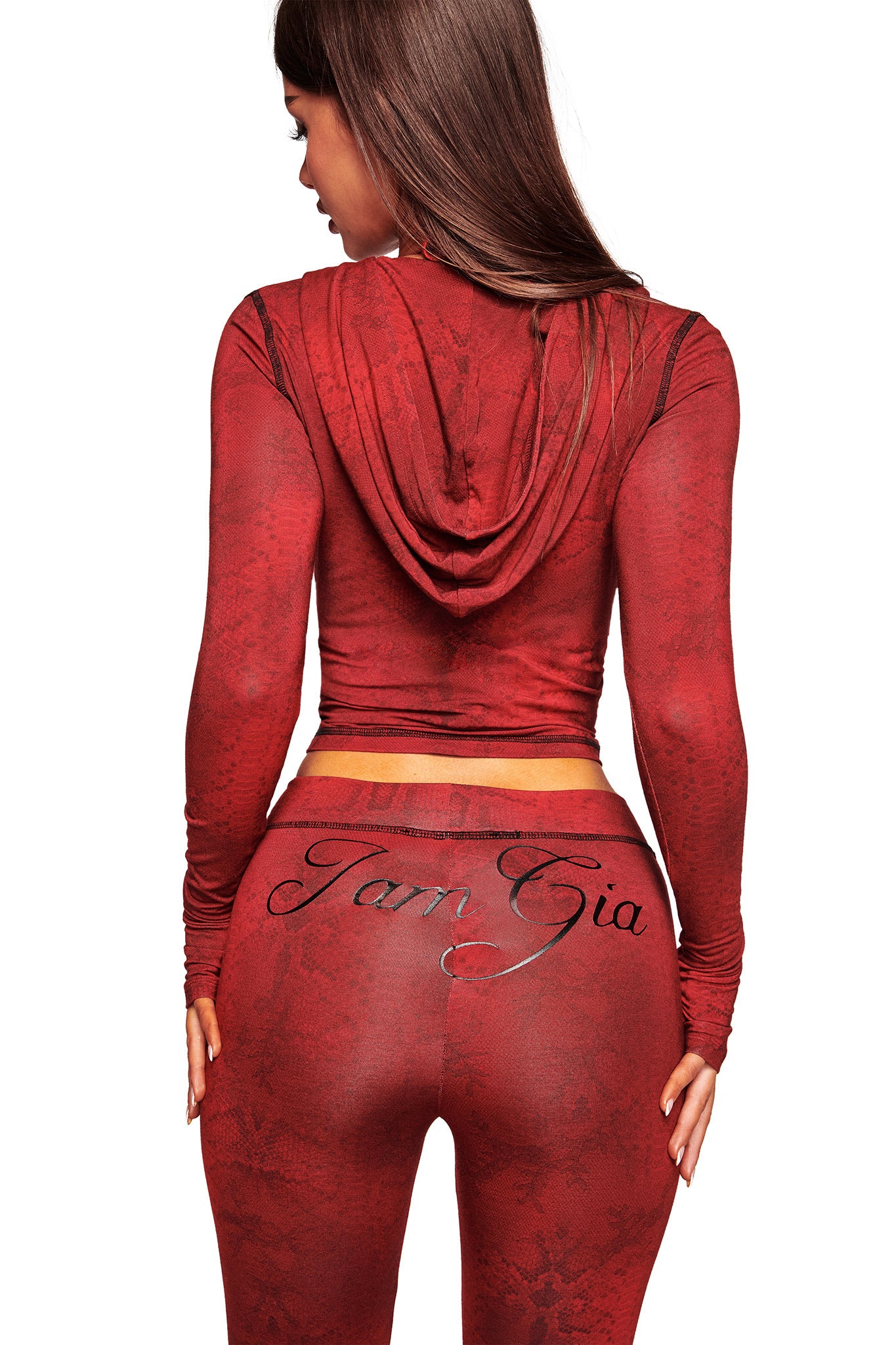 A woman with long brown hair, seen from behind, wears a fitted BLARE HOODIE - RED SERPENTINE by I.AM.GIA and matching leggings. "JamGia" is printed in script across the back of her leggings.