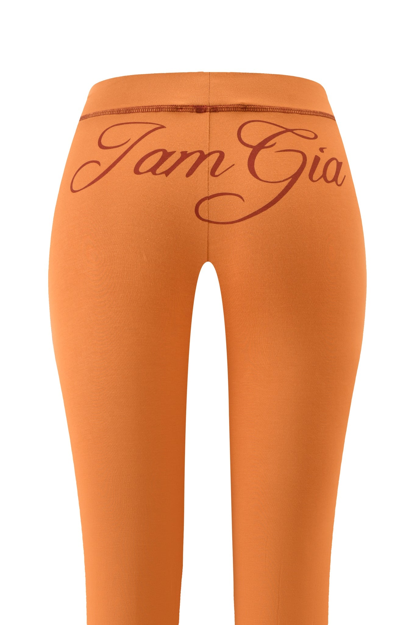 The BLARE TRACKPANT - PUMPKIN by I.AM.GIA features a low-rise waist, viewed from the back with bold pumpkin spice "I.AM.GIA" lettering in large cursive across the waistband.