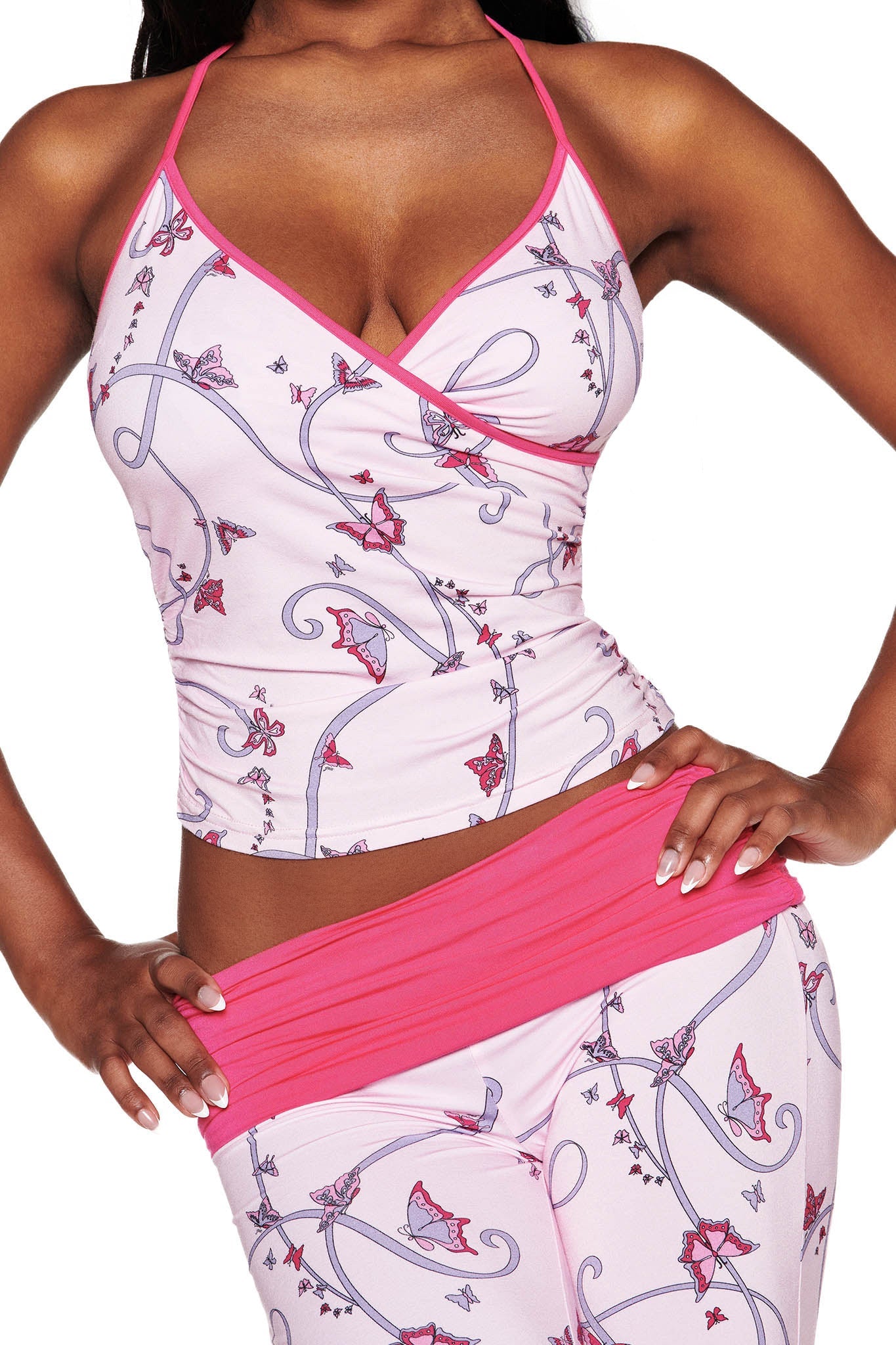 A woman confidently poses with one hand on her hip, wearing the I.AM.GIA JANNIS PANT - PINK : BUTTERFLY RIBBON set. This outfit includes a sleeveless floral and butterfly ribbon top with matching wrap-style leggings featuring pink borders and a mid-rise waist.