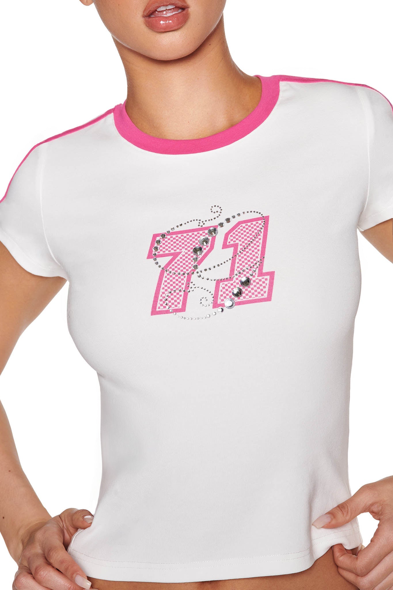 A person wearing the I.AM.GIA JENNIE TOP in WHITE: HOT PINK, featuring rhinestone and floral adorned "71" graphic on a baby tee with pink trim. The bodycon fit enhances their silhouette as they confidently rest their hands on their hips.