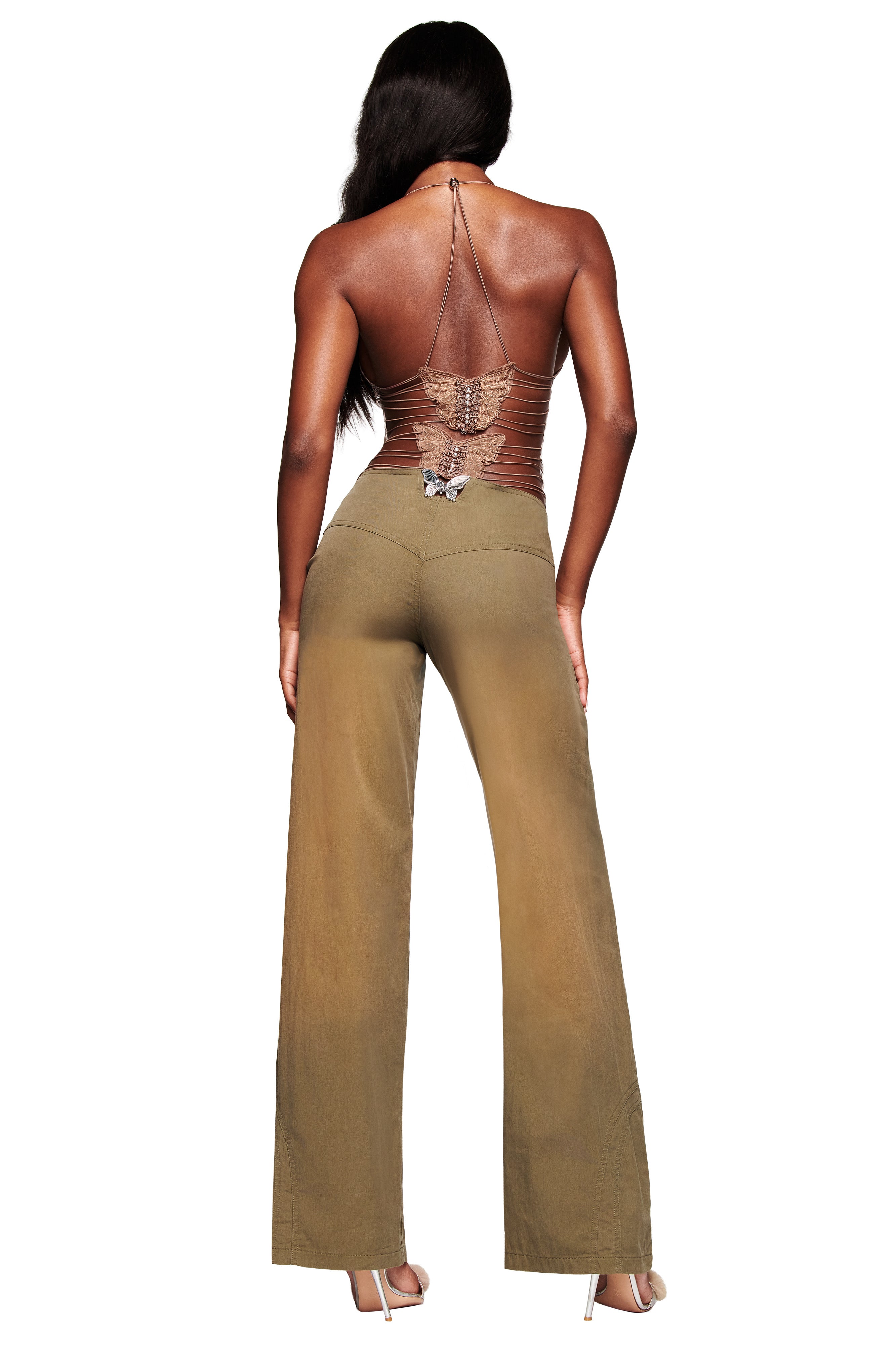 A woman with long dark hair, wearing high heels and a brown halter top with a butterfly design on the back, is seen from behind in the I.AM.GIA SEQUOIA PANT in army green.