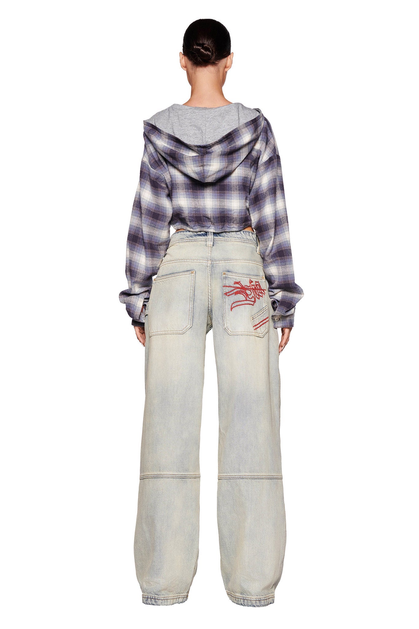 A person with their hair tied back stands facing away, wearing the I.AM.GIA TIFF JACKET in blue over a gray shirt, and faded wide-leg jeans with visible back pockets and red graffiti-style designs on the right side. The eclectic streetwear ensemble channels I.AM.GIA vibes effortlessly.