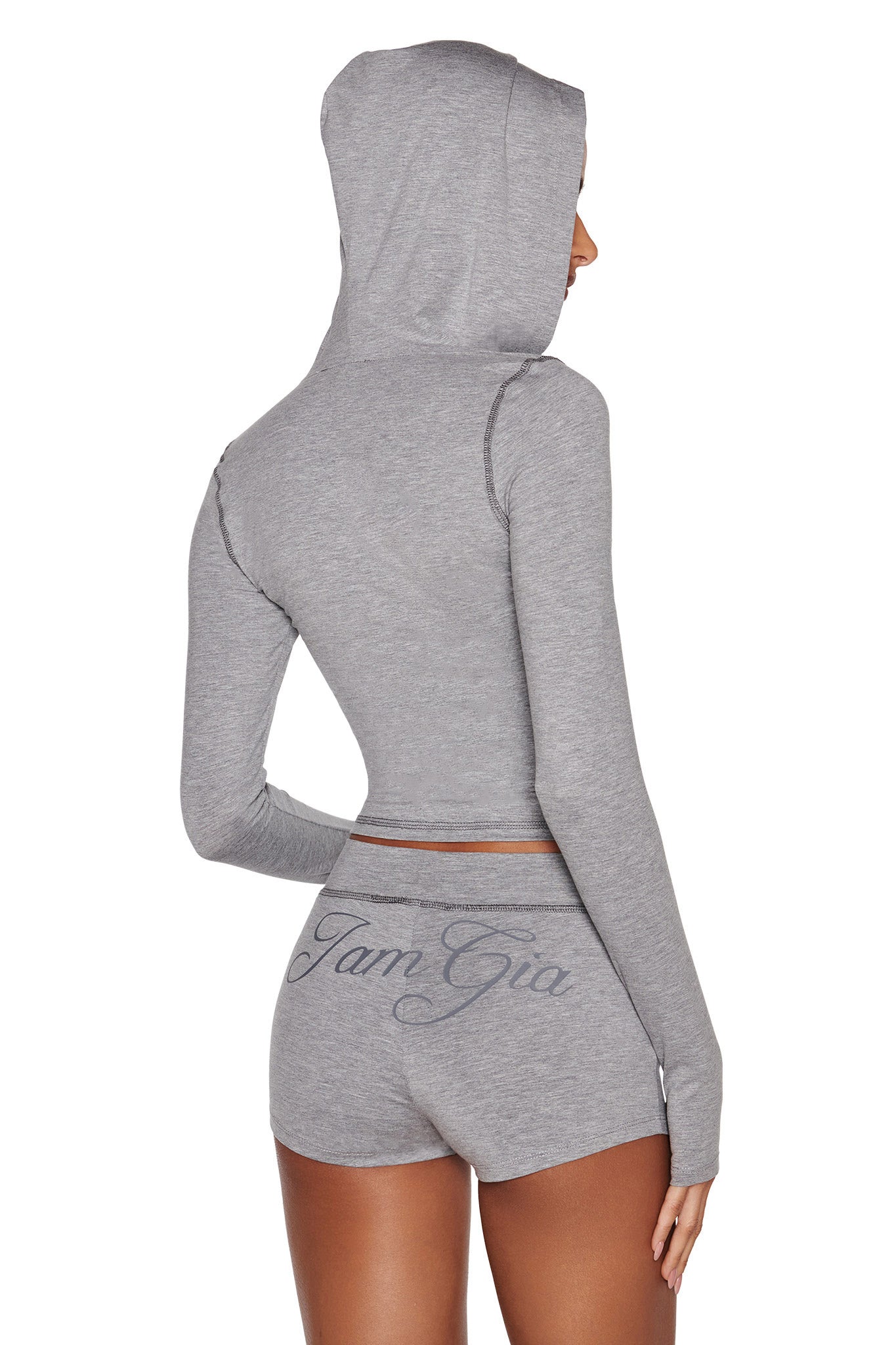 A woman is seen from behind in a fitted, long-sleeve, grey hooded top and matching BLARE JERSEY SHORT - GREY: HEATHER GREY by I.AM.GIA. The bodycon shorts feature "I.AM.GIA" across the back for a bold, sporty look.