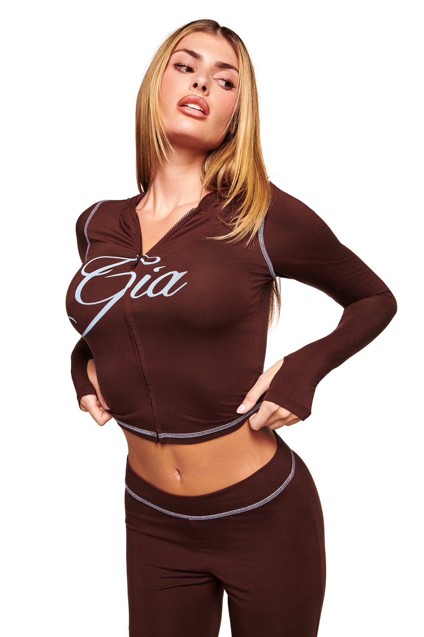 A woman poses with her hands on her hips against a white background, wearing the I.AM.GIA BLARE HOODIE in brown, a long-sleeve two-piece outfit.
