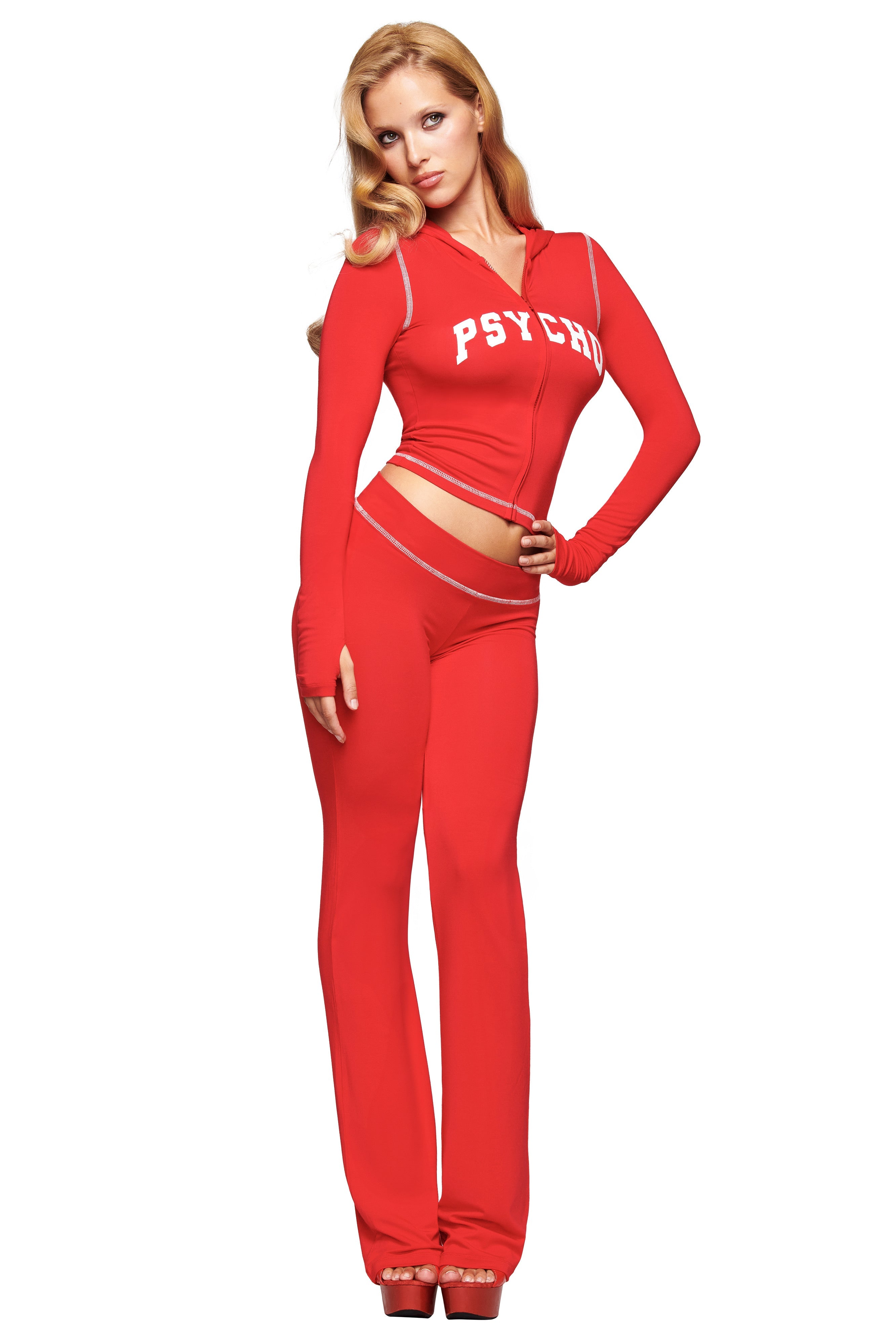 A woman models the I.AM.GIA BLARE HOODIE - RED : PSYCHO : SALSA, featuring "PSYCHO" on the front. The look includes long sleeves, flared pants, and waist cutouts, set against a white background.