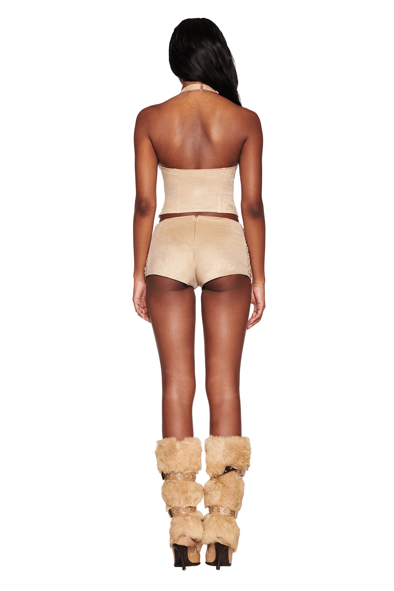 A person is seen from the back in I.AM.GIA's RAMONA SHORT - BEIGE : TAN and a light tan halter top, styled with furry tan boots. This fashion-forward outfit plays on modern design with texture contrast, while decorative lace-up details add a chic touch against the plain white backdrop.