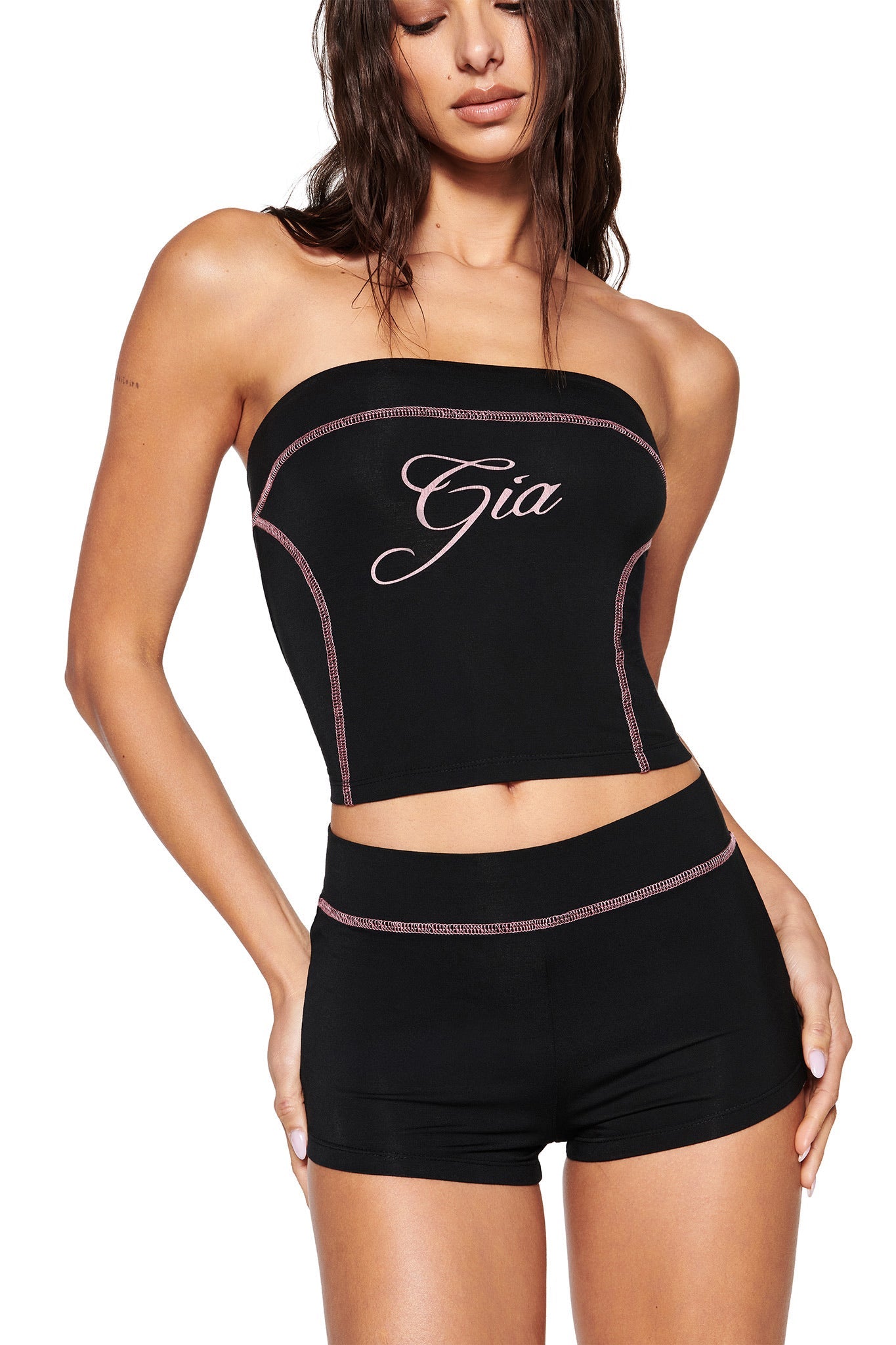 A woman poses in I.AM.GIA's BLARE SHORT - BLACK and a black strapless bodycon top with "Gia" written in cursive, standing against a plain white backdrop with long, wet-look hair.