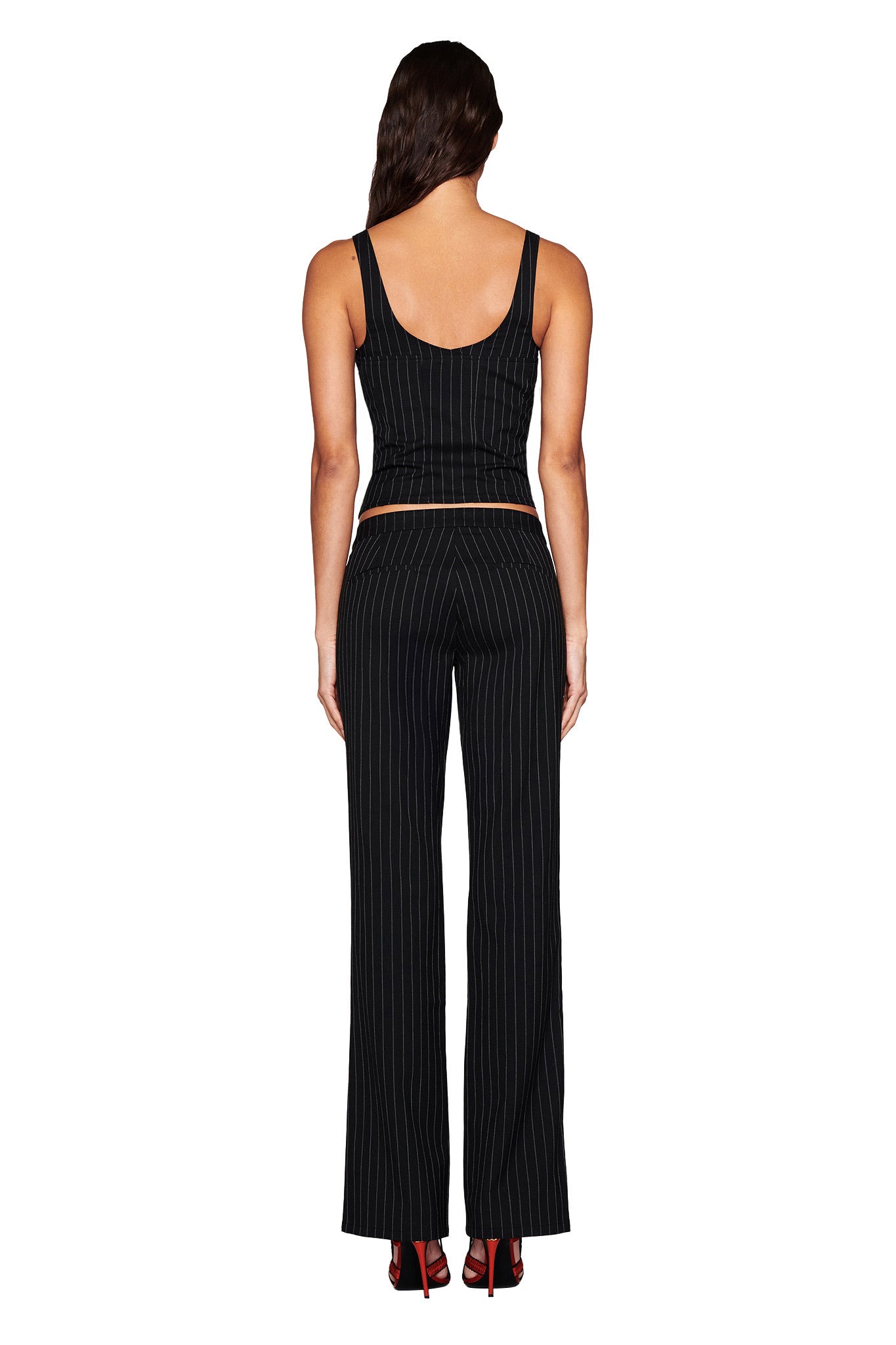 A person with long hair, facing away, is dressed in a black pinstripe sleeveless top and I.AM.GIA's MARRION PANT - BLACK. The straight-leg pants feature a low-rise waist, providing a chic look against a plain white background.