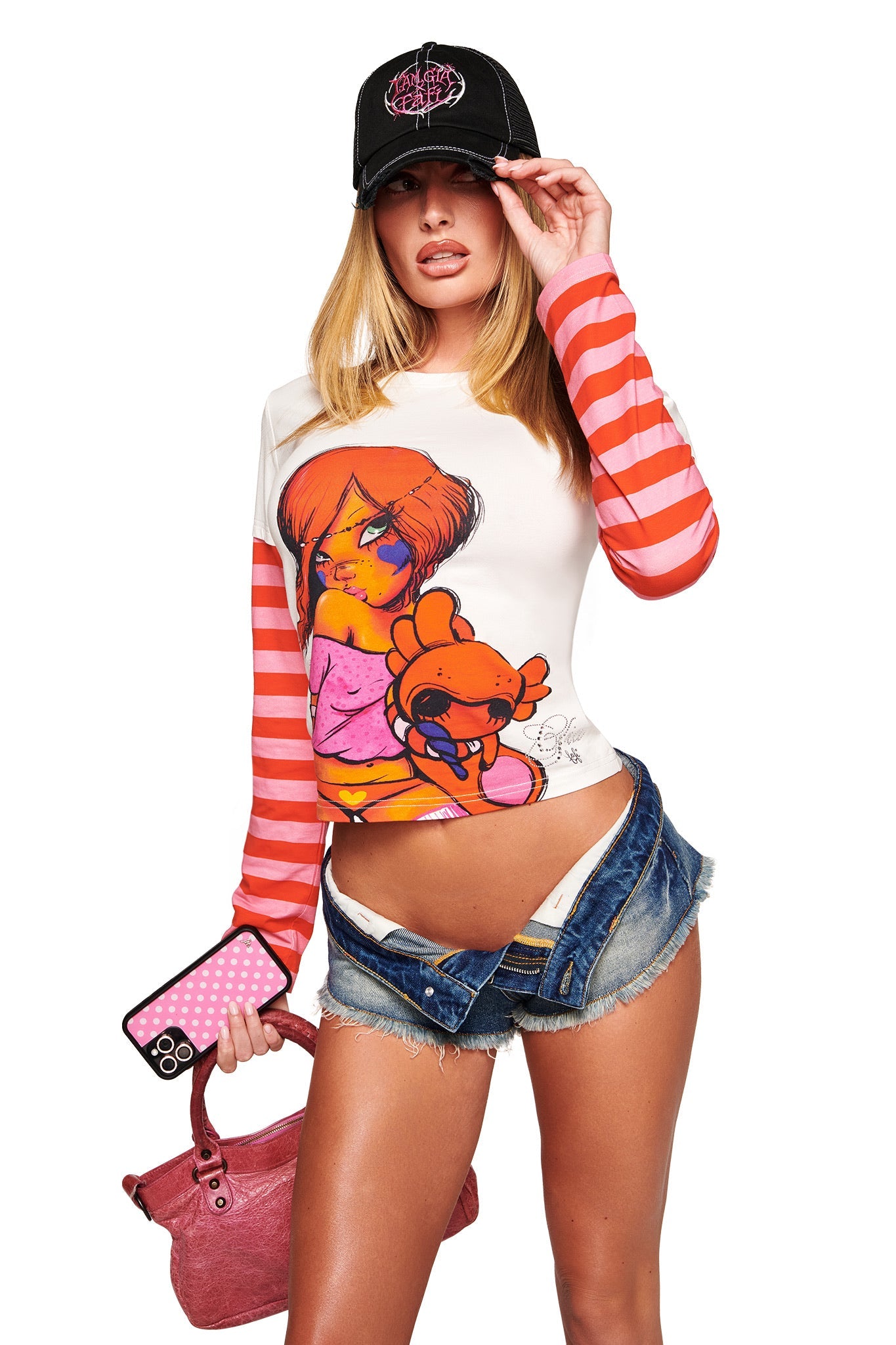 A woman poses in the I.AM.GIA FAFI DOUBLE LAYER TEE - WHITE with stripes and cartoon graphic, denim shorts, a black cap, pink handbag, and polka dot phone case with diamante logo detailing against a white background.