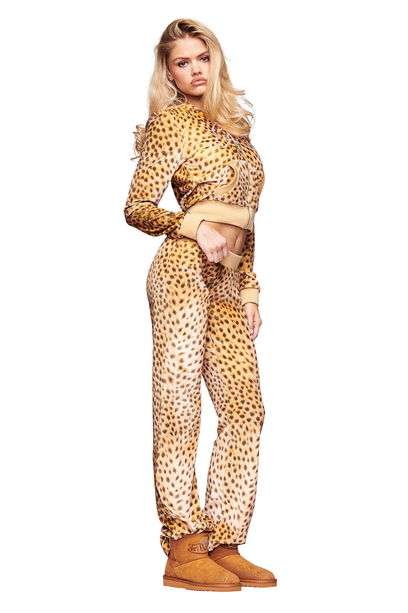 A woman with long blonde hair poses against a white background wearing the I.AM.GIA X VON DUTCH KAMERON VELOUR JACKET in leopard print, paired with matching sweatpants and tan boots.
