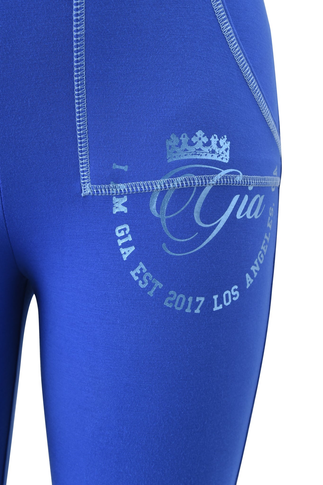 Close-up of a person wearing I.AM.GIA BLARE FORM POCKET TRACKPANT - COBALT FOIL, featuring sculpted Form fabric, visible stitching, and a metallic "Gia EST 2017 LOS ANGELES" foil logo with a crown graphic.