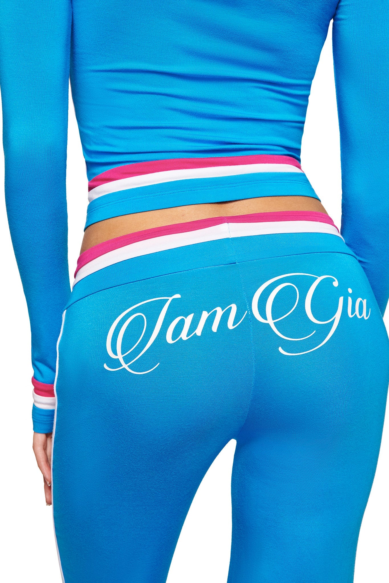Wearing I.AM.GIA’s BLARE STRIPED TRACKPANT in sky blue, featuring colorful stripes at the low rise waist and “I AM GIA” in white cursive on the back. The photo highlights the lower back and legs.