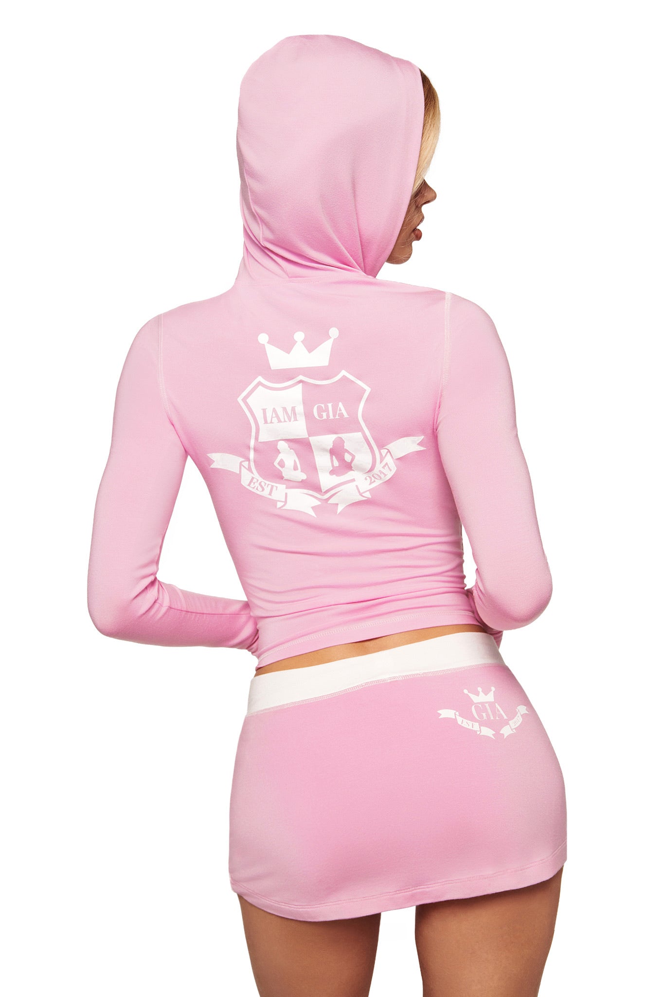 A person is seen from behind wearing a pink hooded crop top and the I.AM.GIA BLARE PIPING MICRO SKORT in baby pink and white, featuring white crest designs on the back.