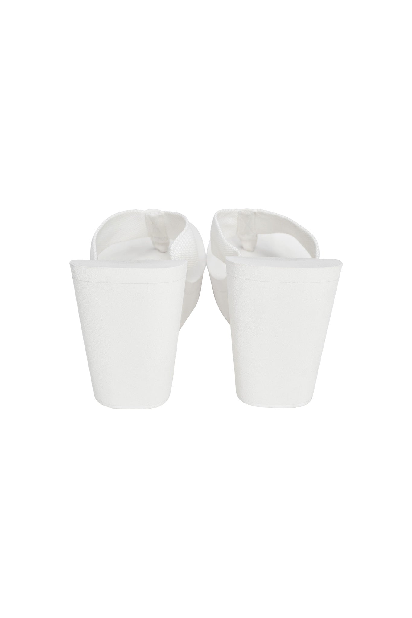 Rear view of a pair of I.AM.GIA SHELBY FLIP FLOP - WHITE, featuring thick soles and white straps. The shoes are standing upright, showcasing the elevated platform and simple, minimalist design against a white background.