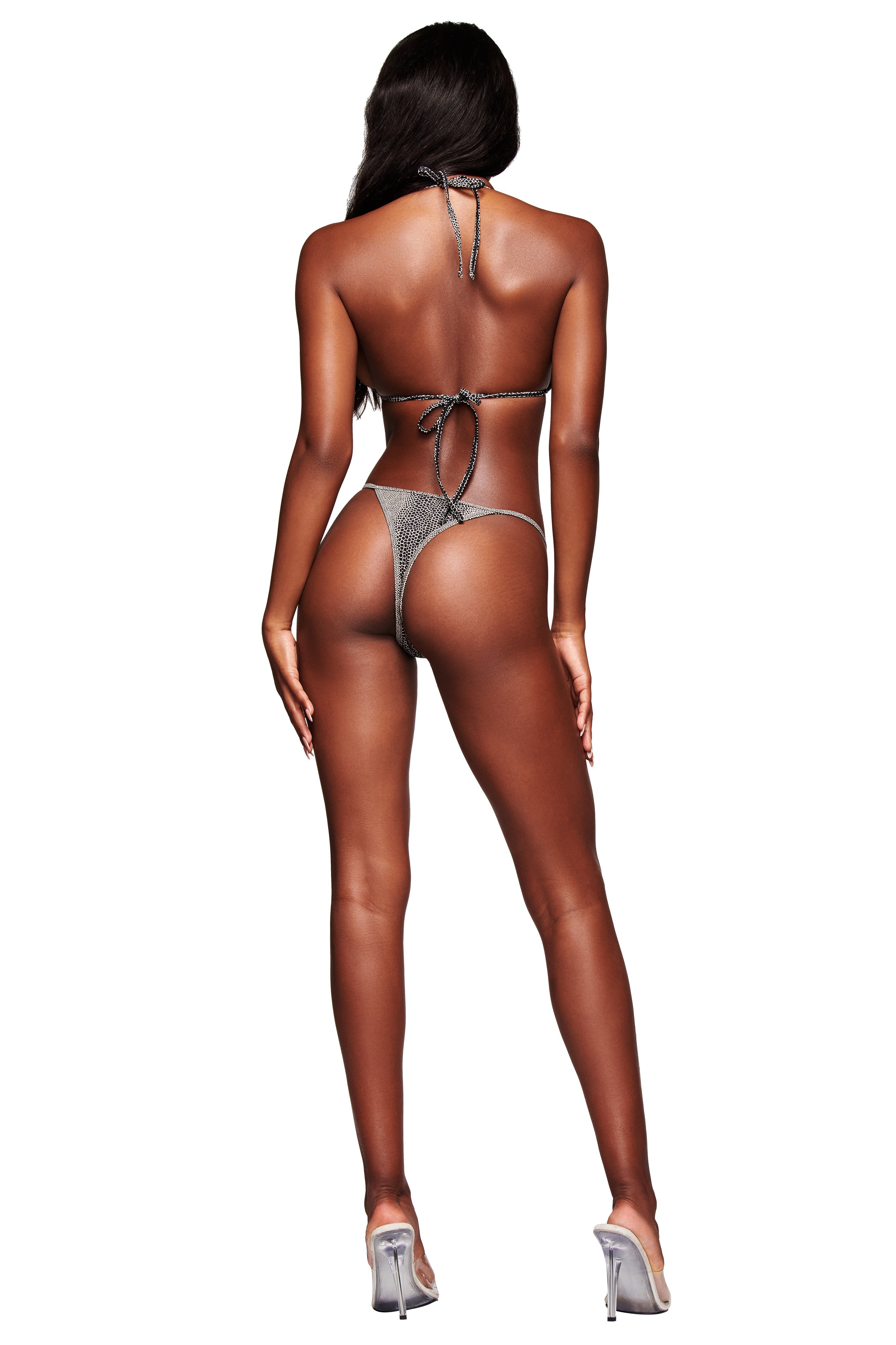 A woman models the I.AM.GIA AVA BIKINI TOP - SERPICO, standing with her back to the camera against a white background. She wears clear high heels, her long hair down, and her arms relaxed by her sides.