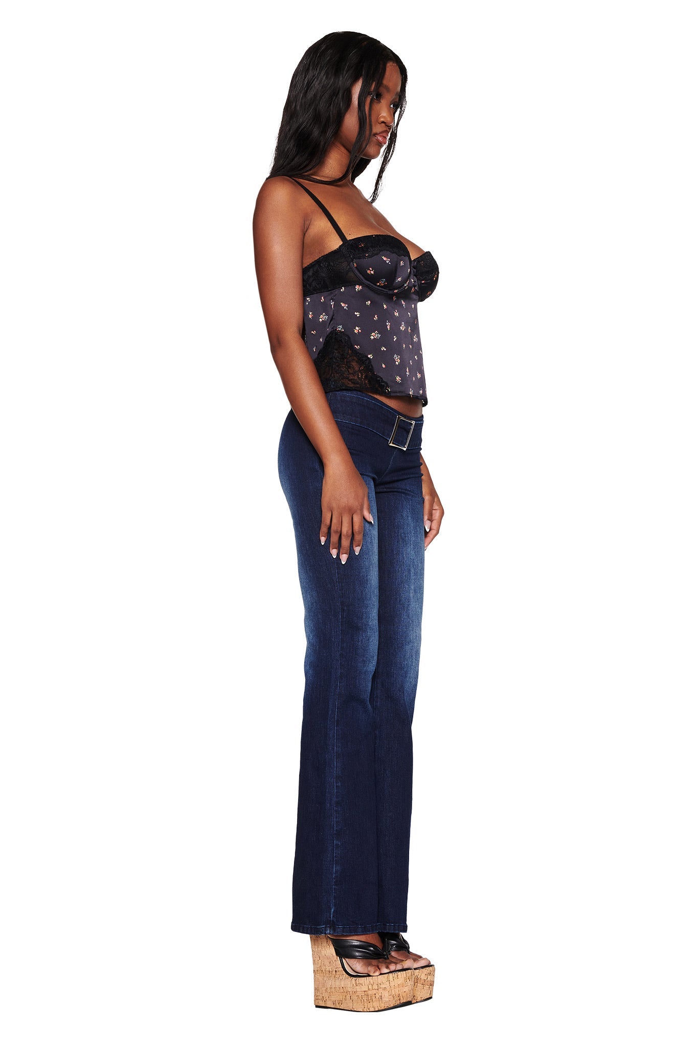 Against a white backdrop, a woman stands in profile wearing the vintage-inspired LUELLA CAMI TOP in DITSY FLORAL by I.AM.GIA and dark blue jeans. Her look is finished with wooden wedge sandals, and her long hair flows elegantly down her back.