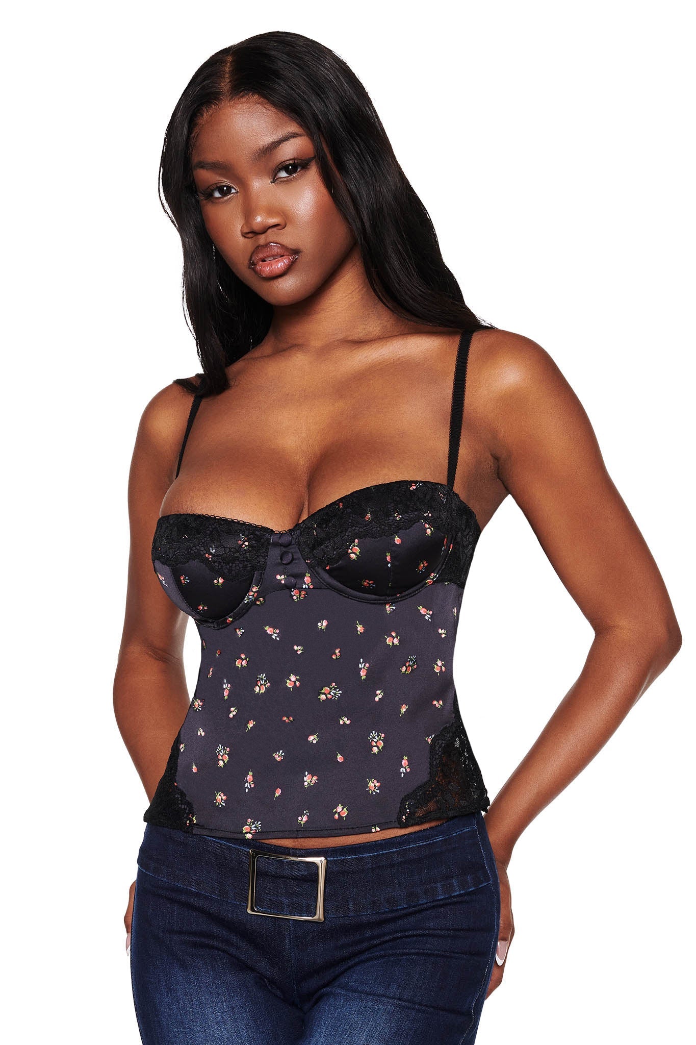 A woman models the LUELLA CAMI TOP - BLACK : DITSY FLORAL by I.AM.GIA, a fitted piece with spaghetti straps and lace detailing, paired with dark jeans and a belt against a pristine white background.