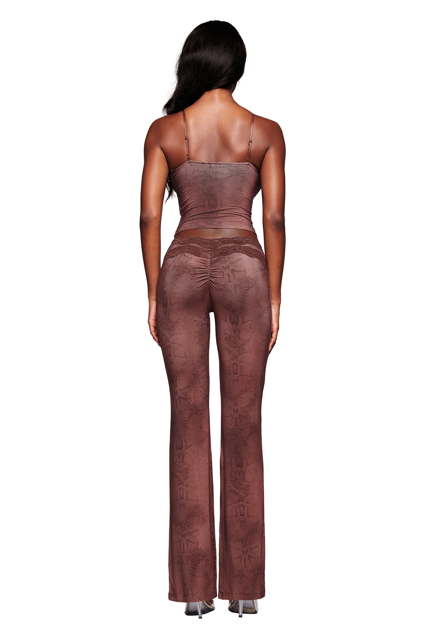 A woman with long, wavy dark hair stands facing away against a white background, wearing the fitted BEAU TOP - BROWN and matching high-waisted, flared pants by I.AM.GIA, both featuring a subtle pattern.