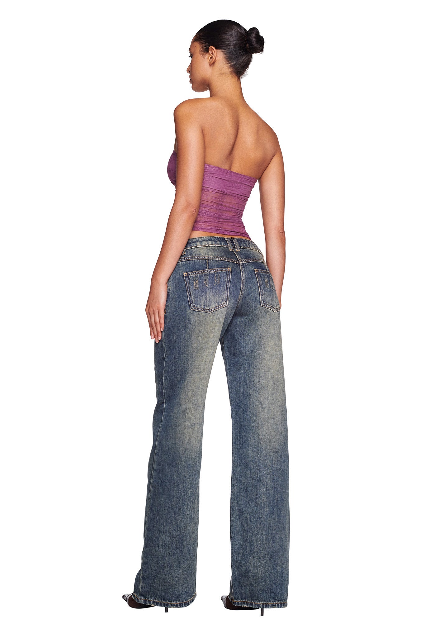 A person is styled in a strapless purple top and the DYLAN JEAN - BLUE DENIM by I.AM.GIA, featuring low-waisted denim jeans with a relaxed wide-leg fit. Their hair is elegantly pulled into a bun as they pose against a plain white background, accentuating the subtle sandblasting detail on the jeans.