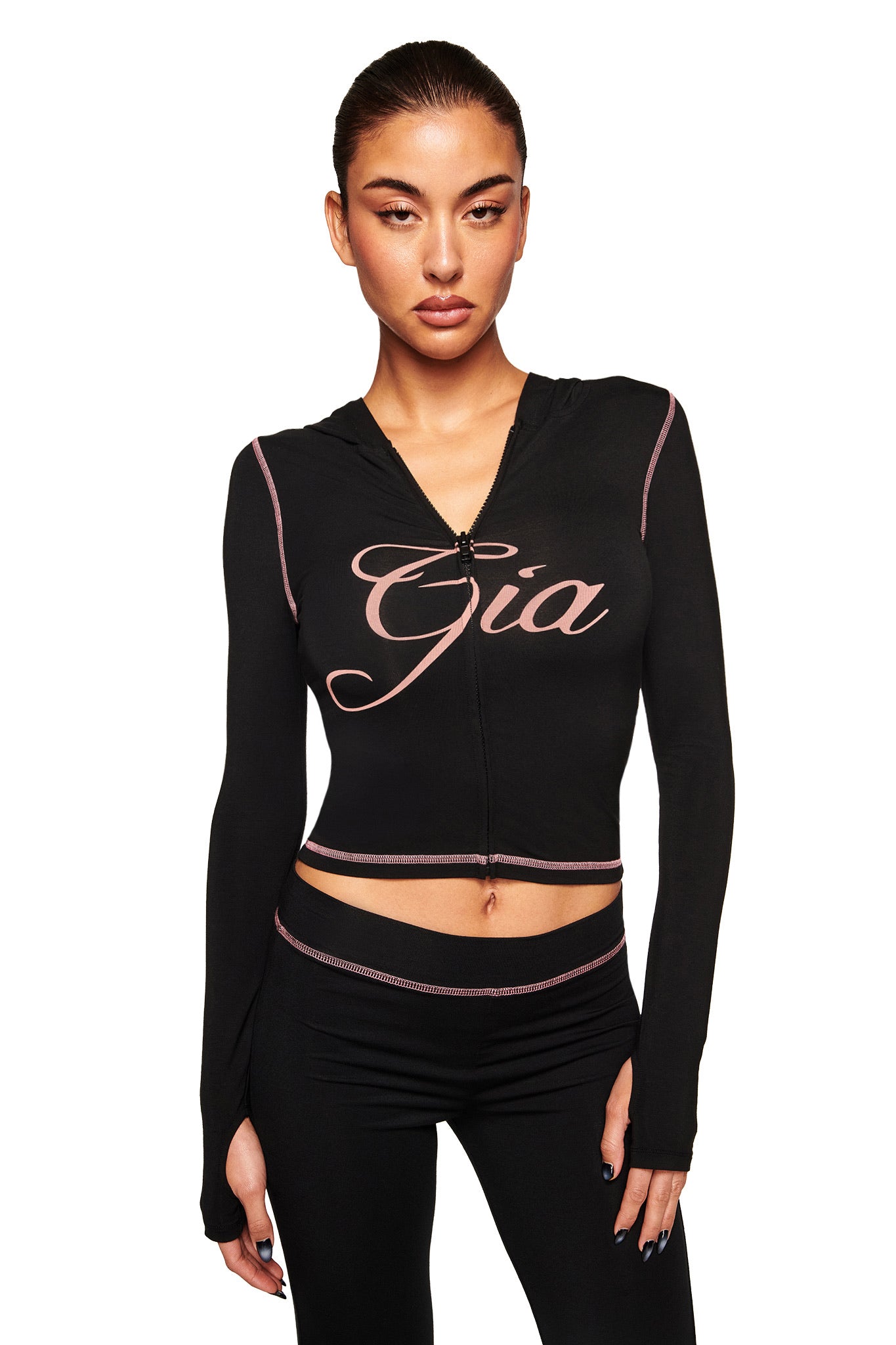 Model wears the I.AM.GIA BLARE HOODIE - BLACK, featuring "Gia" in bold script on the front, matched with black leggings, and poses against a plain white background.