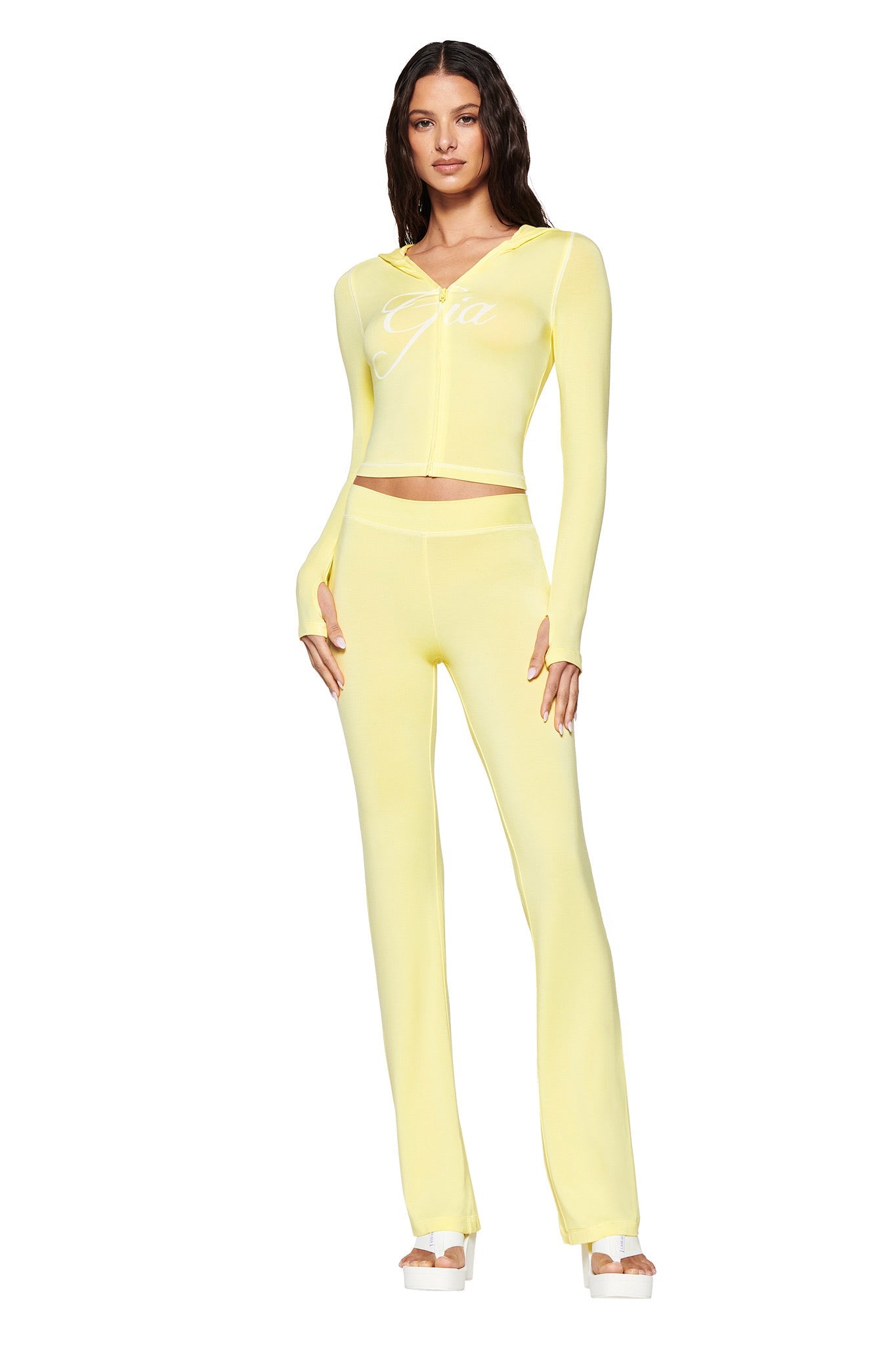 A woman wears a pale yellow outfit with an I.AM.GIA long-sleeve top and BLARE TRACKPANT. She's paired it with white platform sandals against a white background.