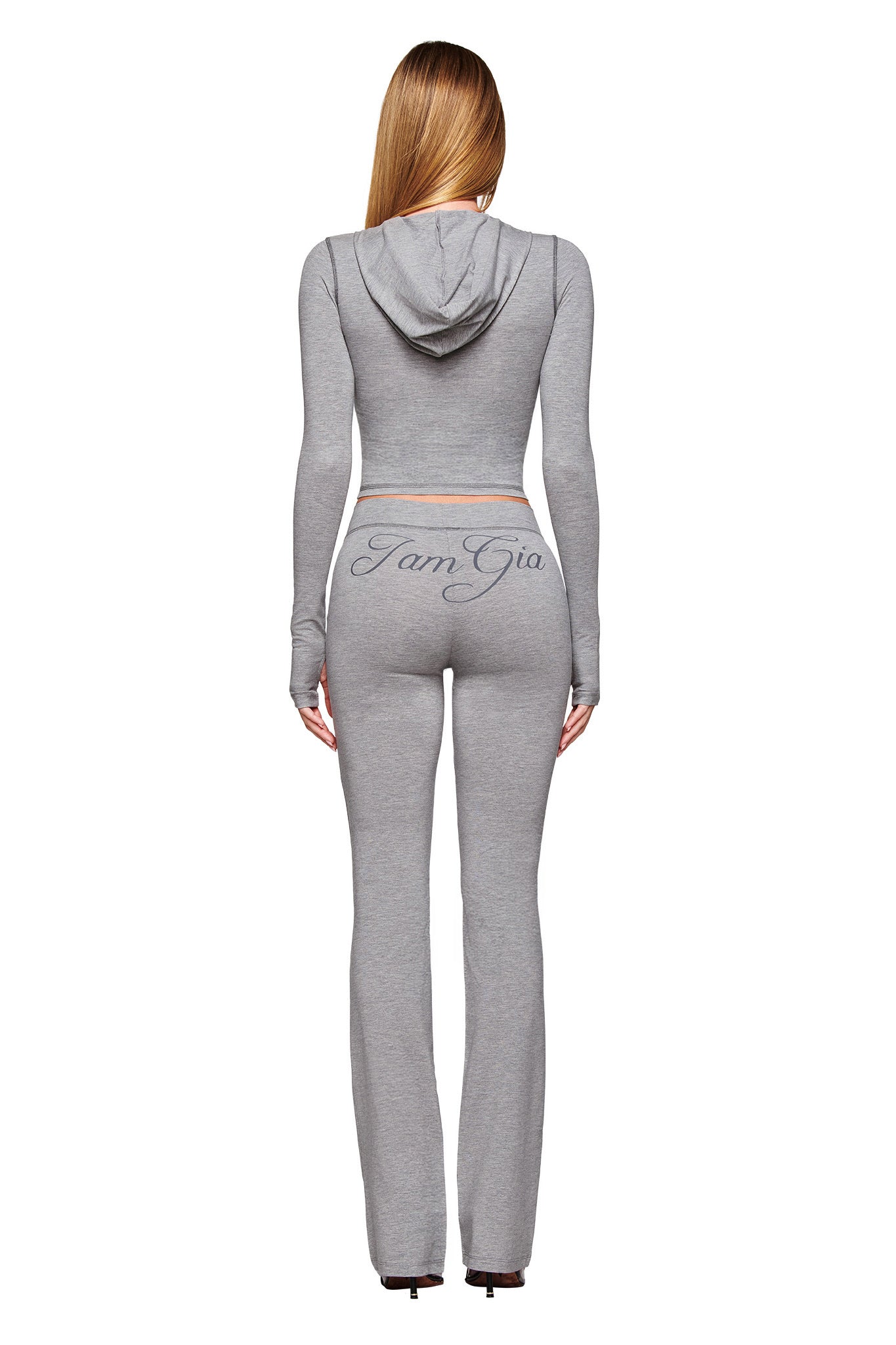 A woman with long, straight blonde hair is seen from the back wearing a fitted heather grey hooded crop top and matching BLARE JERSEY TRACKPANT - GREY by I.AM.GIA, featuring flared legs and “IamGia” in cursive on the back.