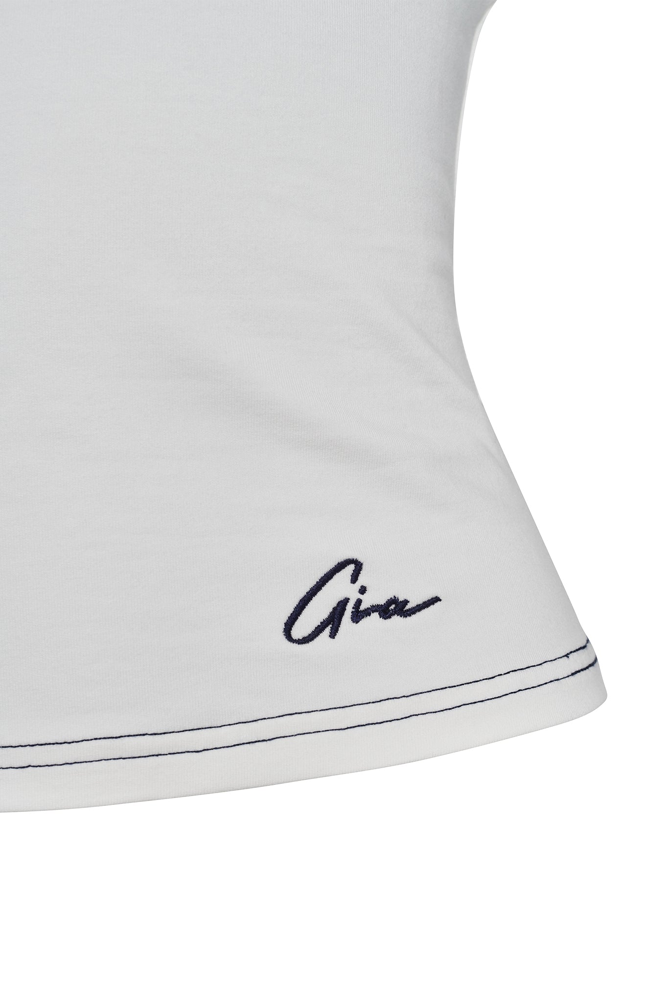 Close-up of the EDITA TOP - WHITE by I.AM.GIA, featuring a dark blue stitched signature at the bottom that reads "I.AM.GIA." The hem is detailed with a dark blue stitch along the edge. The fabric appears smooth and fitted.