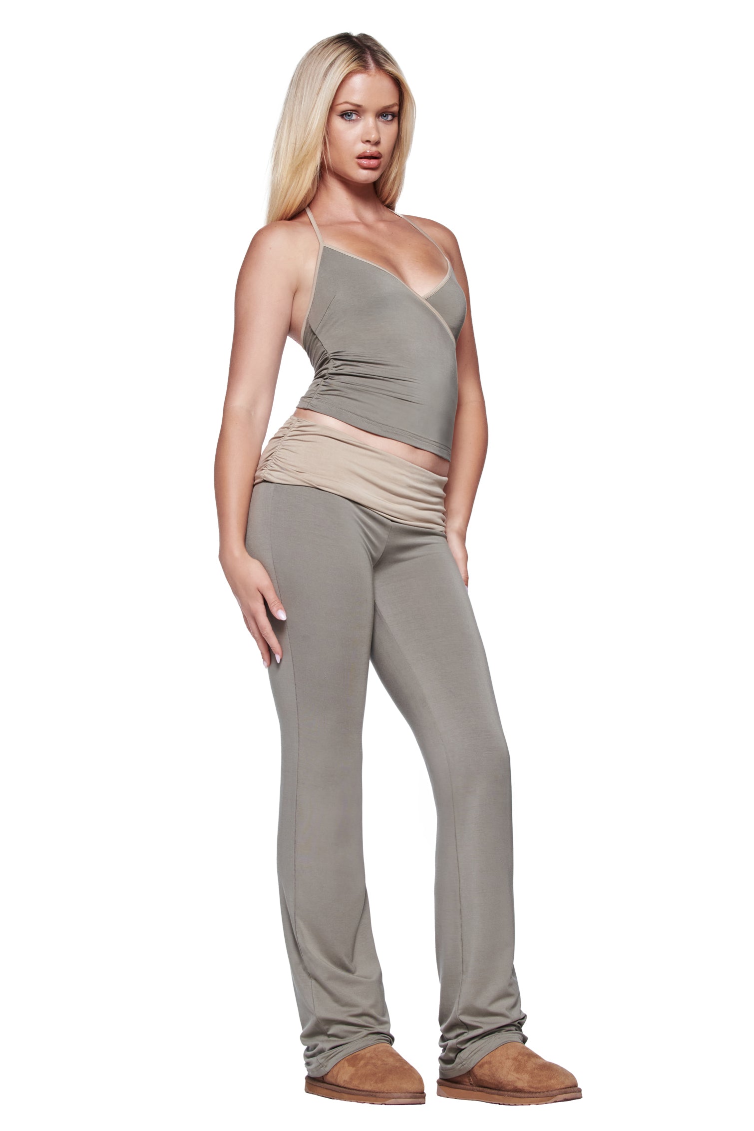 A woman with long blonde hair poses in the I.AM.GIA JANNIS TANK in green, featuring spaghetti straps and a wrapped waist, paired with matching fitted pants and brown shoes against a white background.