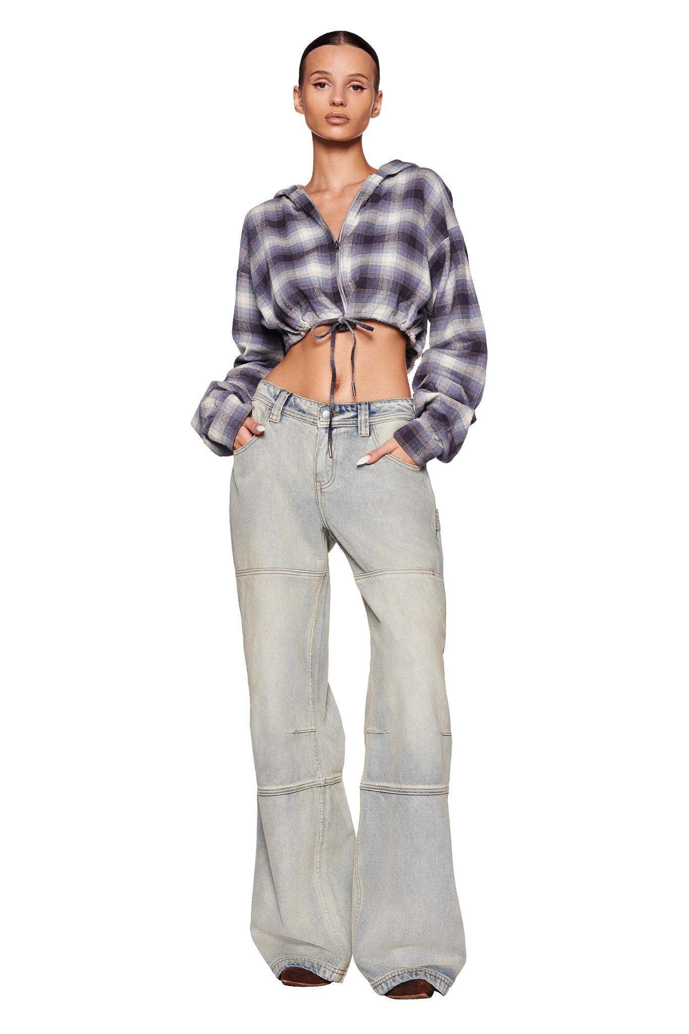 A woman with a tight bun hairstyle is sporting the TIFF JACKET - BLUE from I.AM.GIA, paired with light blue high-waisted wide-leg jeans. She has her hands in her pockets and stands against a plain white background.