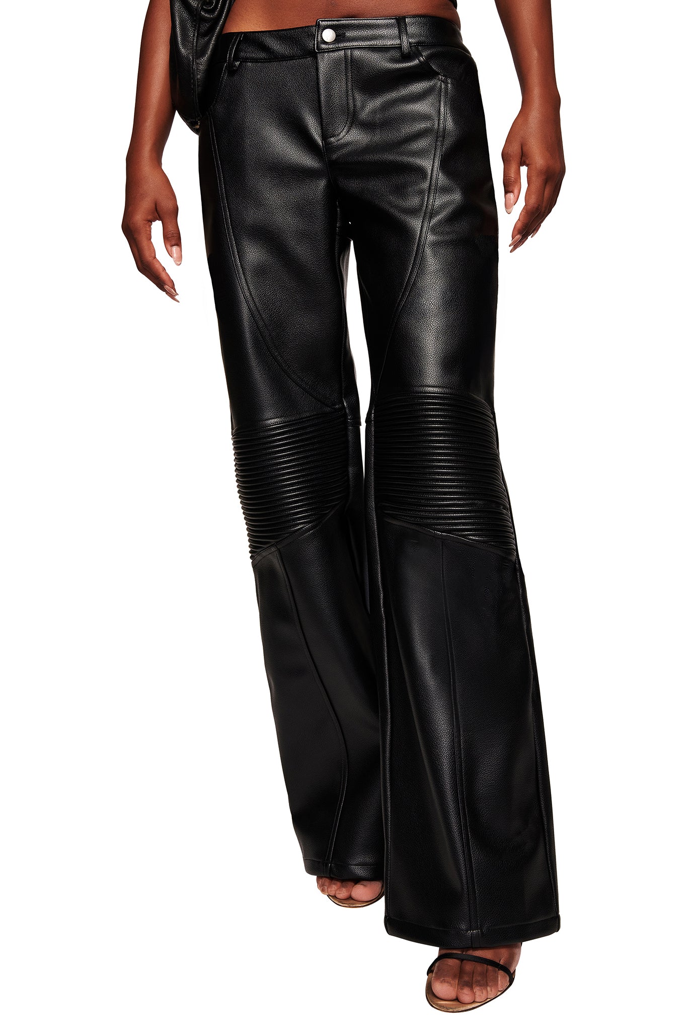 A person wears the I.AM.GIA KRISTIE PANT in black—high-waisted, wide-leg moto pants with ribbed detailing above the knees—styled with open-toe sandals. Only their lower half is visible.