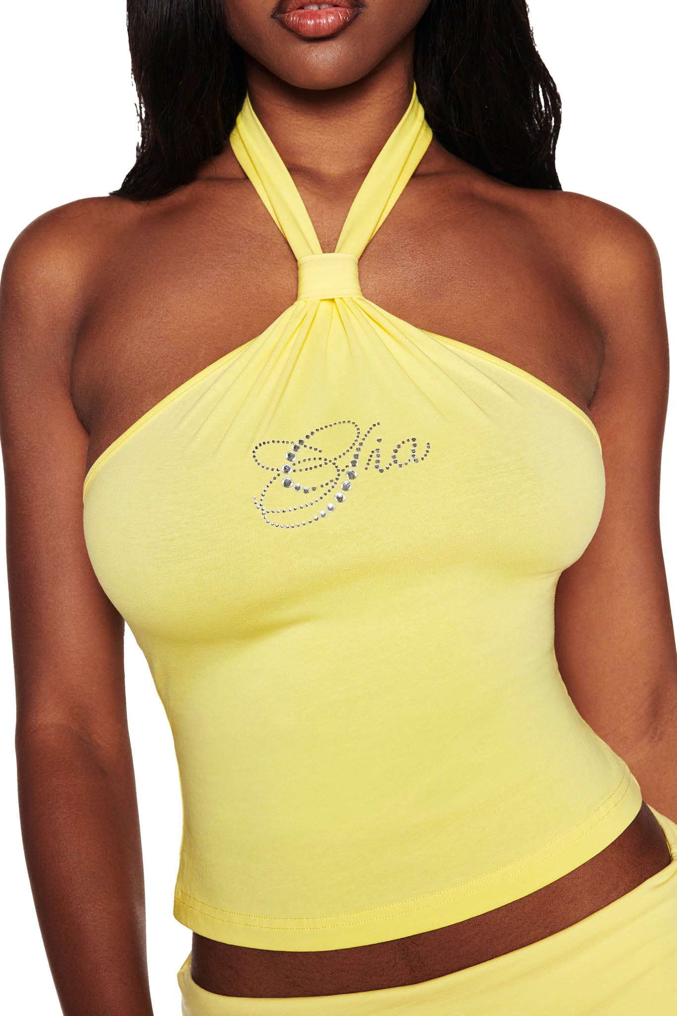 Someone wearing the ROWAN TOP - YELLOW by I.AM.GIA, featuring a halter neck and rhinestone embellishments spelling "Gia" on the front.