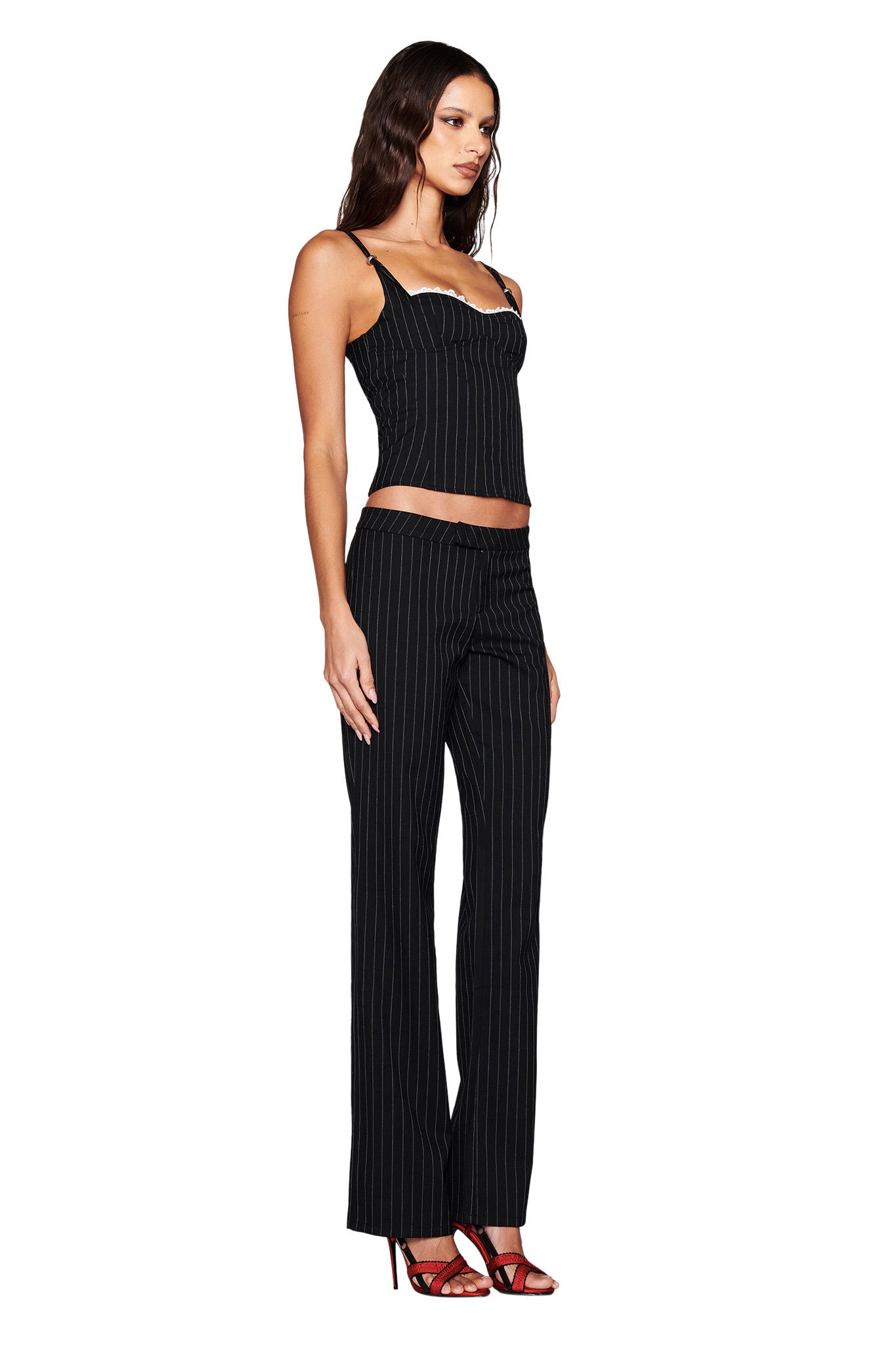 A woman showcases the chic MARRION PANT in black by I.AM.GIA, styled with a fitted black pinstripe tank and red high-heeled sandals, standing sideways against a white backdrop.