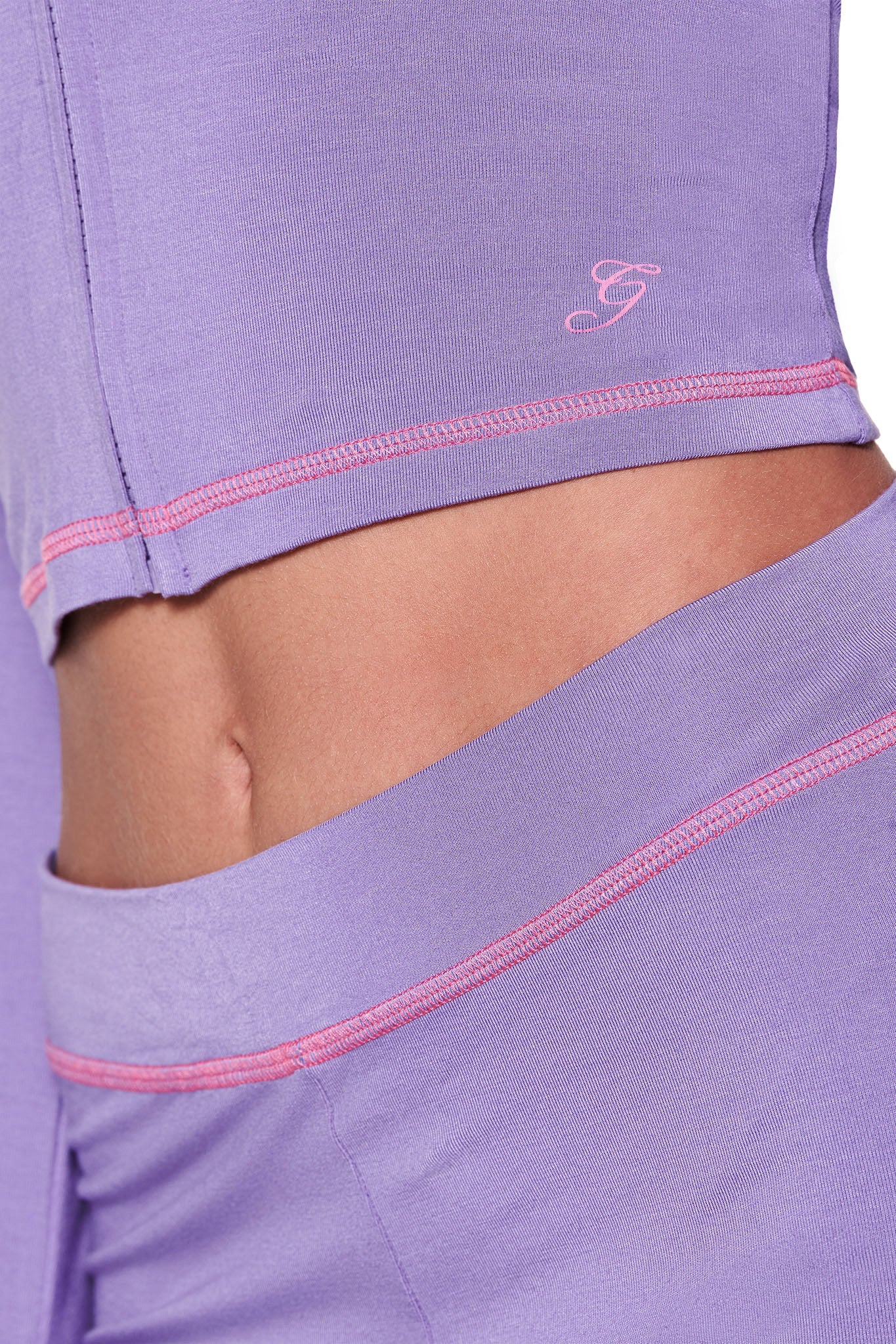 A person wears I.AM.GIA's BLARE HOODIE in purple with pink stitching, highlighting the waistband of leggings and hem of a bodycon top. The smooth, stretchy fabric features a small logo.