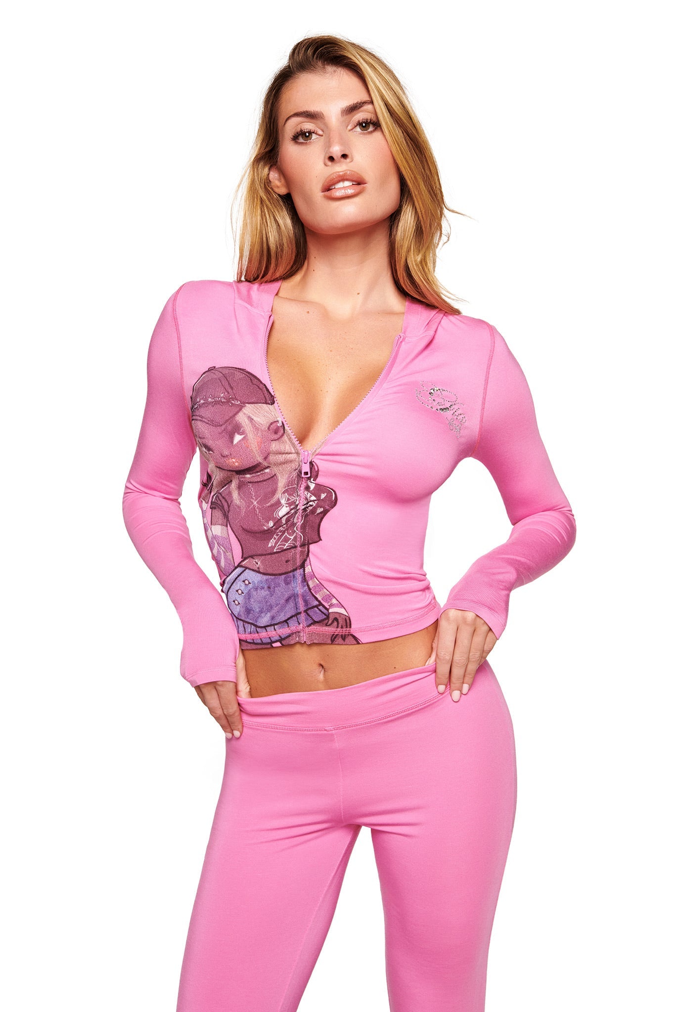 A woman poses confidently in the I.AM.GIA FAFI BLARE HOODIE in bubblegum pink, featuring a fitted, long sleeve design with a deep neckline, illustrated chest graphic, and logo, paired with matching pink pants.