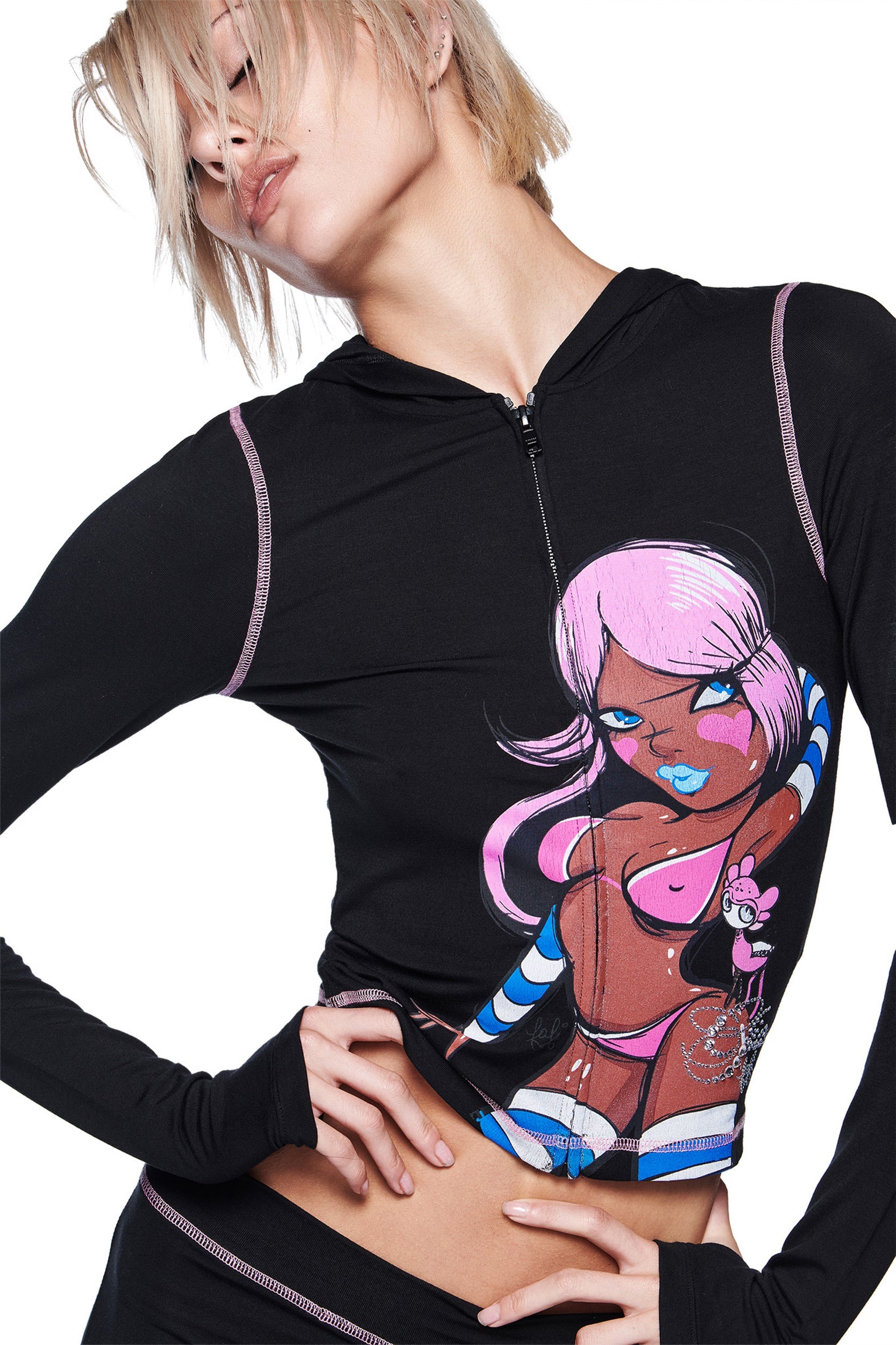 A person with short blonde hair wears the I.AM.GIA FAFI BLARE HOODIE - BLACK, which features an illustrated cartoon woman with pink hair, blue lips, and a pink bikini posing with one hand on her hip against a white background.