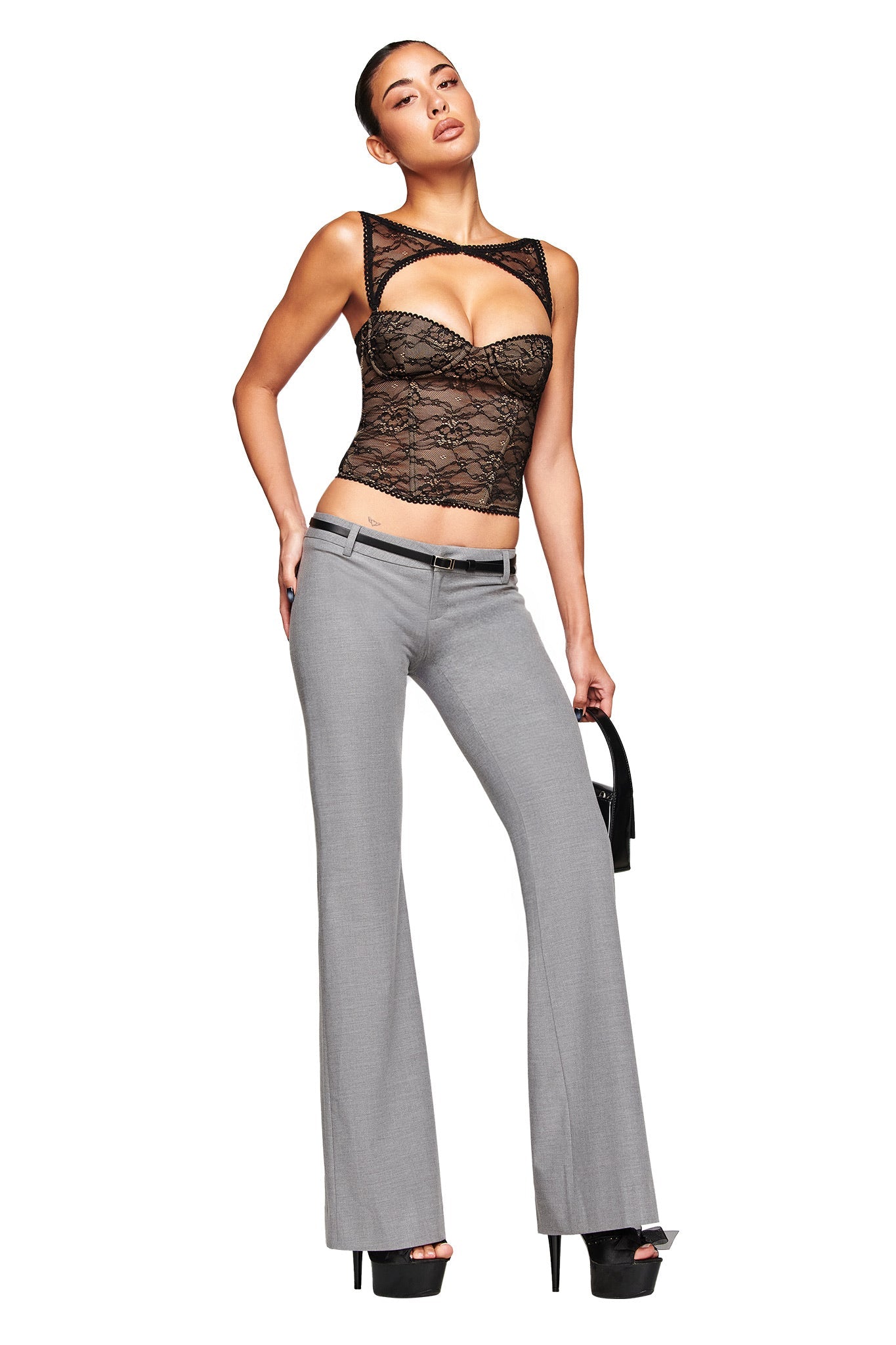 A woman poses confidently in I.AM.GIA's CLARA PANT - GREY, featuring relaxed straight legs and a detachable faux leather belt, paired with black platform heels and a lace bustier top with cut-outs, against a white background.