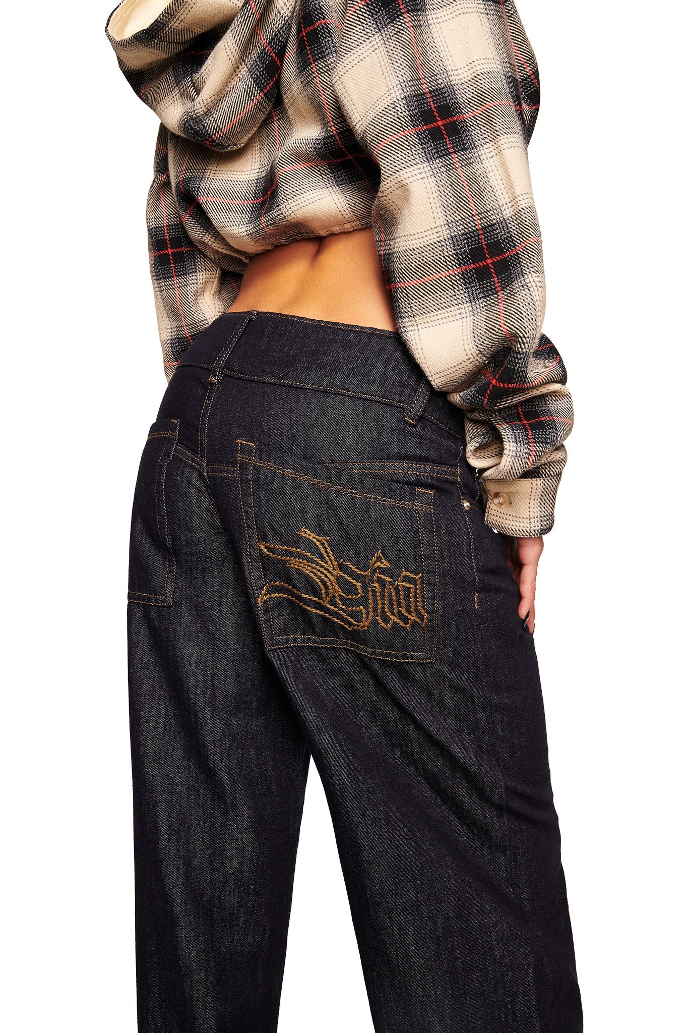 Model wearing I.AM.GIA's MOXIE JEAN - INDIGO, featuring low-rise denim with gold-embroidered back pockets, paired with a cropped plaid hoodie, shown from the back against a white background.
