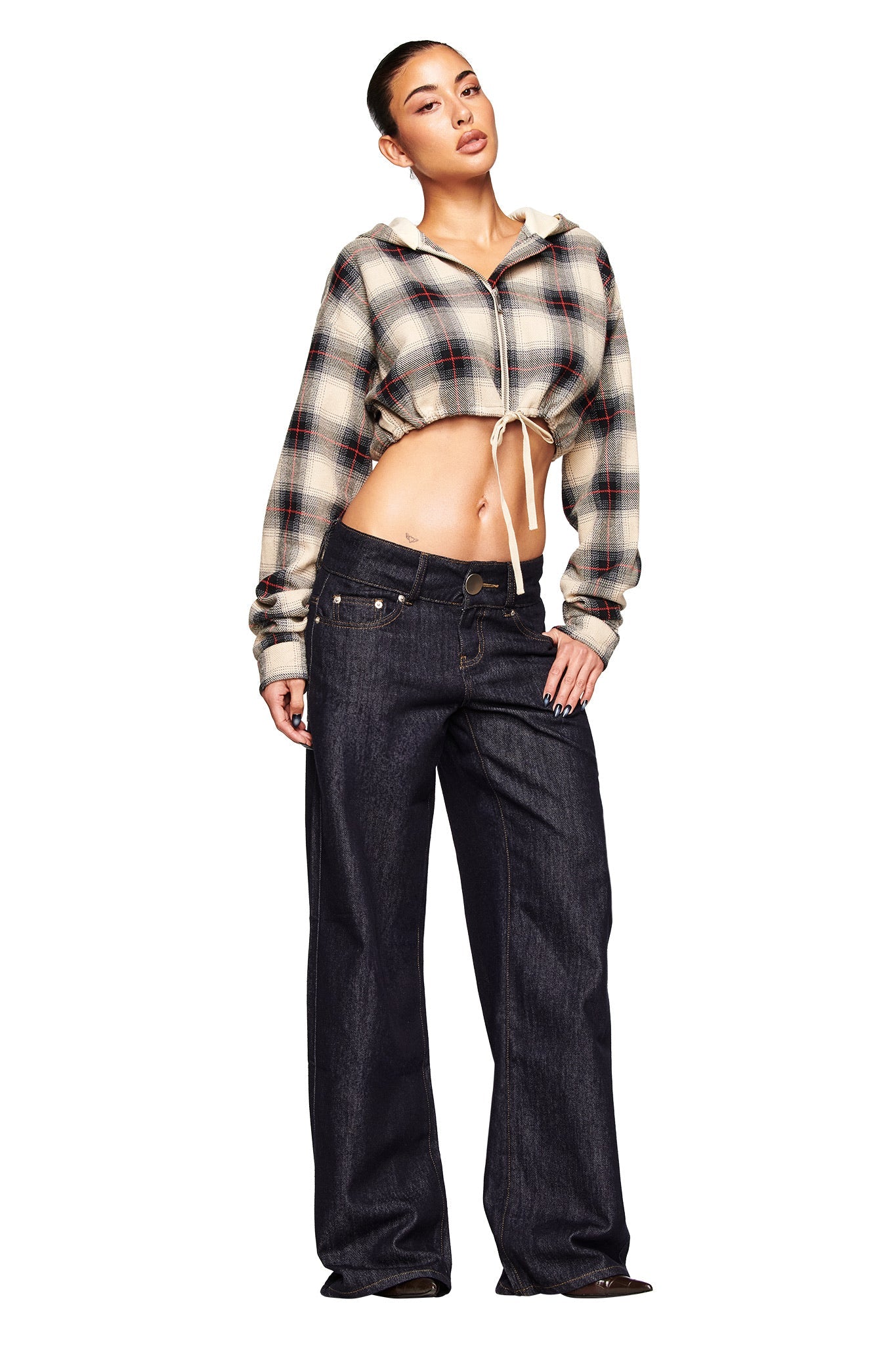 A woman poses confidently in I.AM.GIA's MOXIE JEAN - INDIGO, styled with a cropped plaid zip-up hoodie and set against a plain white background.