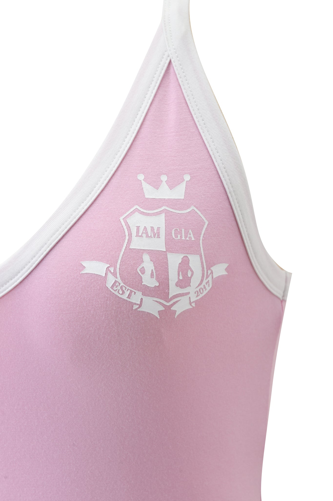 Close-up of the BLARE V-NECK TANK in baby pink and white by I.AM.GIA, featuring a printed white crest with a crown, "I.AM.GIA" text, two figure silhouettes, and "EST 2017" on a banner.