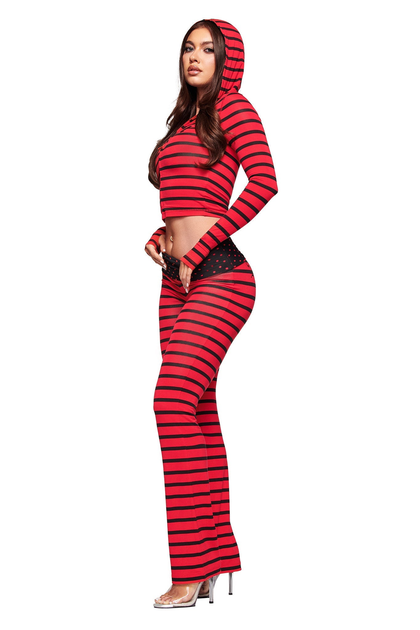 A woman stands in profile wearing the I.AM.GIA BLARE HOODIE in red and black stripes, paired with matching pants featuring a black polka dot waistband and clear high-heeled shoes.