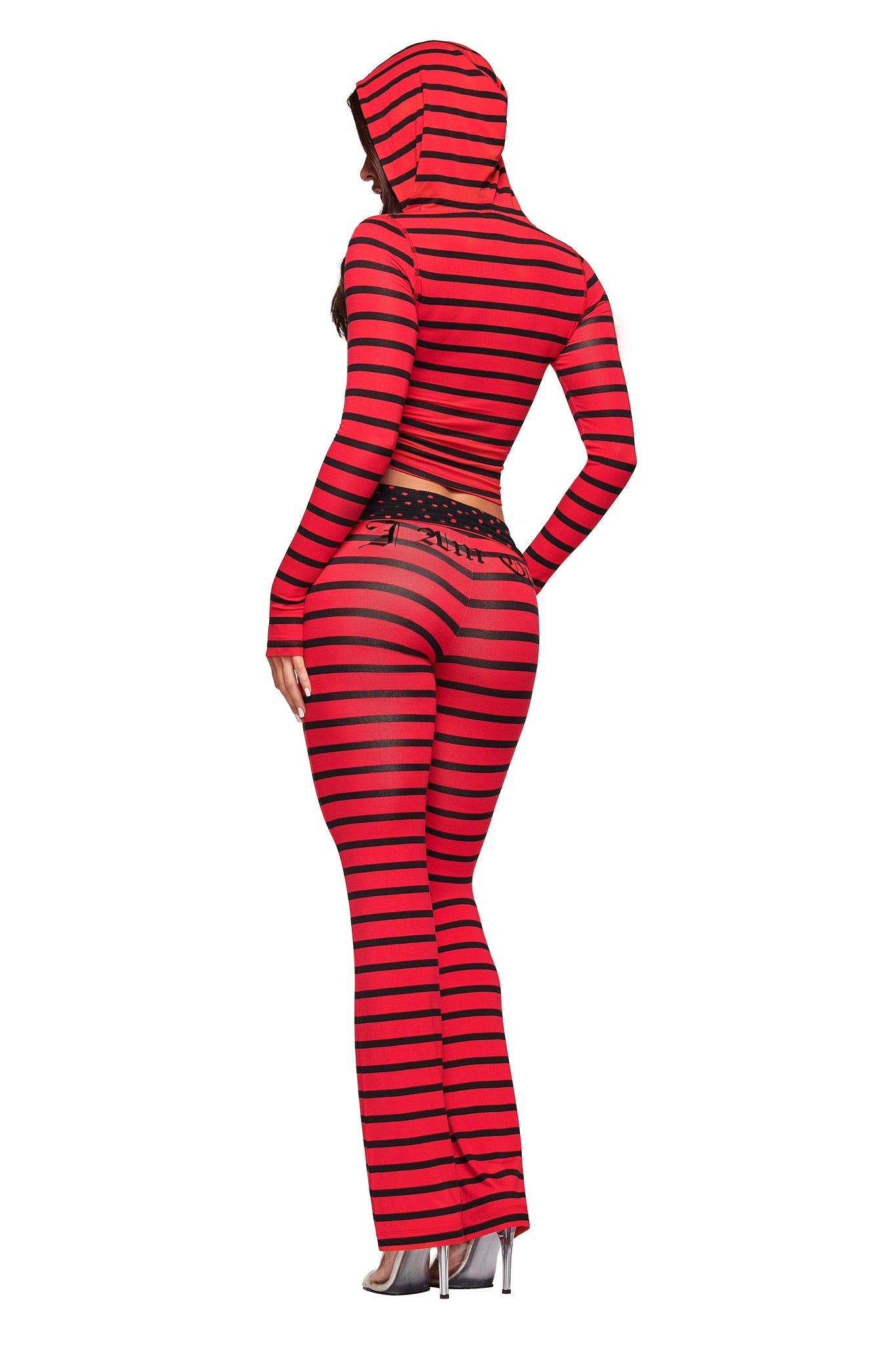 A person wears the I.AM.GIA BLARE HOODIE in red and black stripe with matching viscose, sheer flared pants, standing in heels and facing away from the camera against a white background.