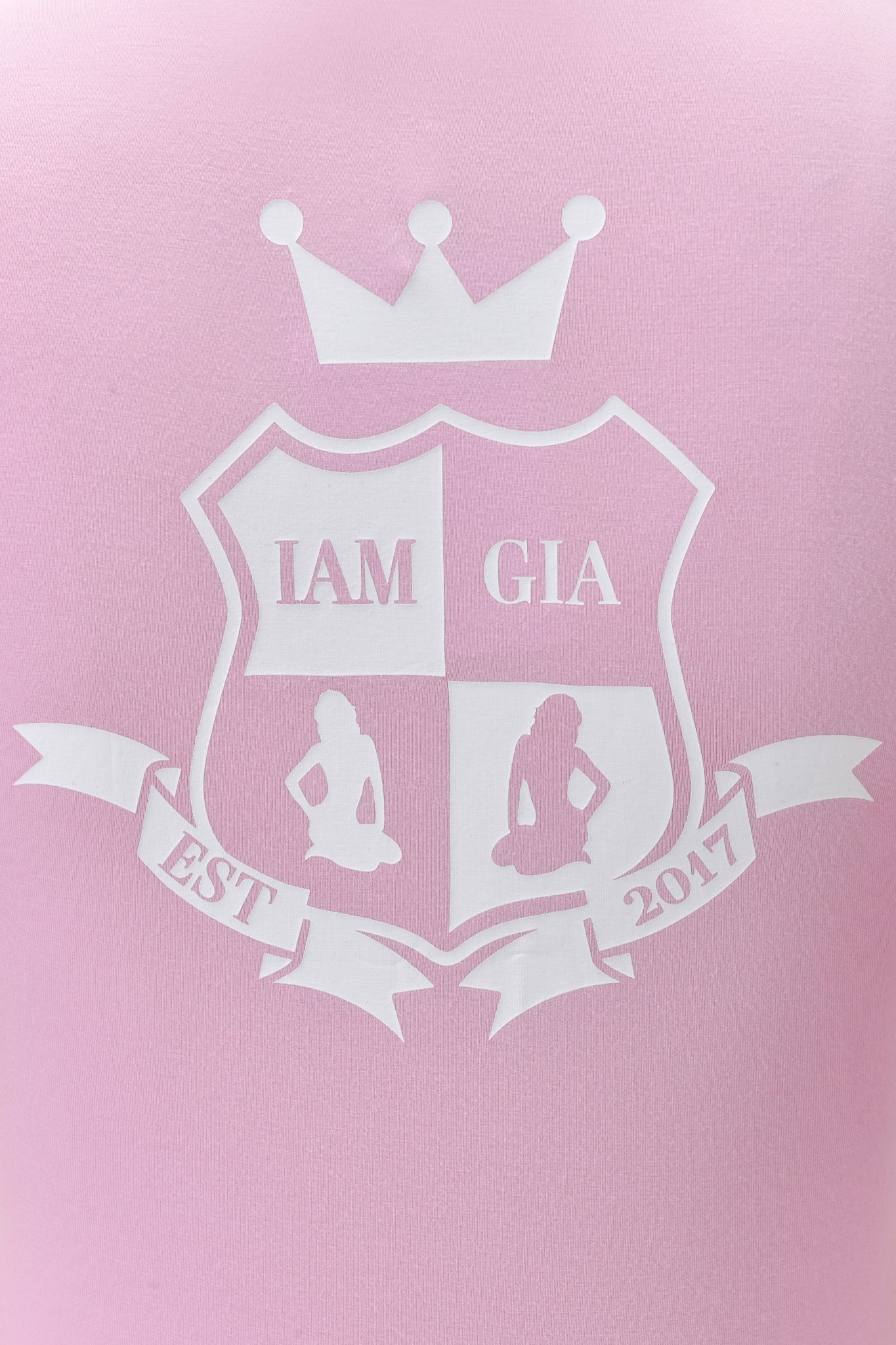 The BLARE PIPING HOODIE in baby pink and white by I.AM.GIA features a sporty backdrop with a white crest, crown, "I.AM.GIA" text, two sitting women silhouettes, and a "EST 2017" ribbon.