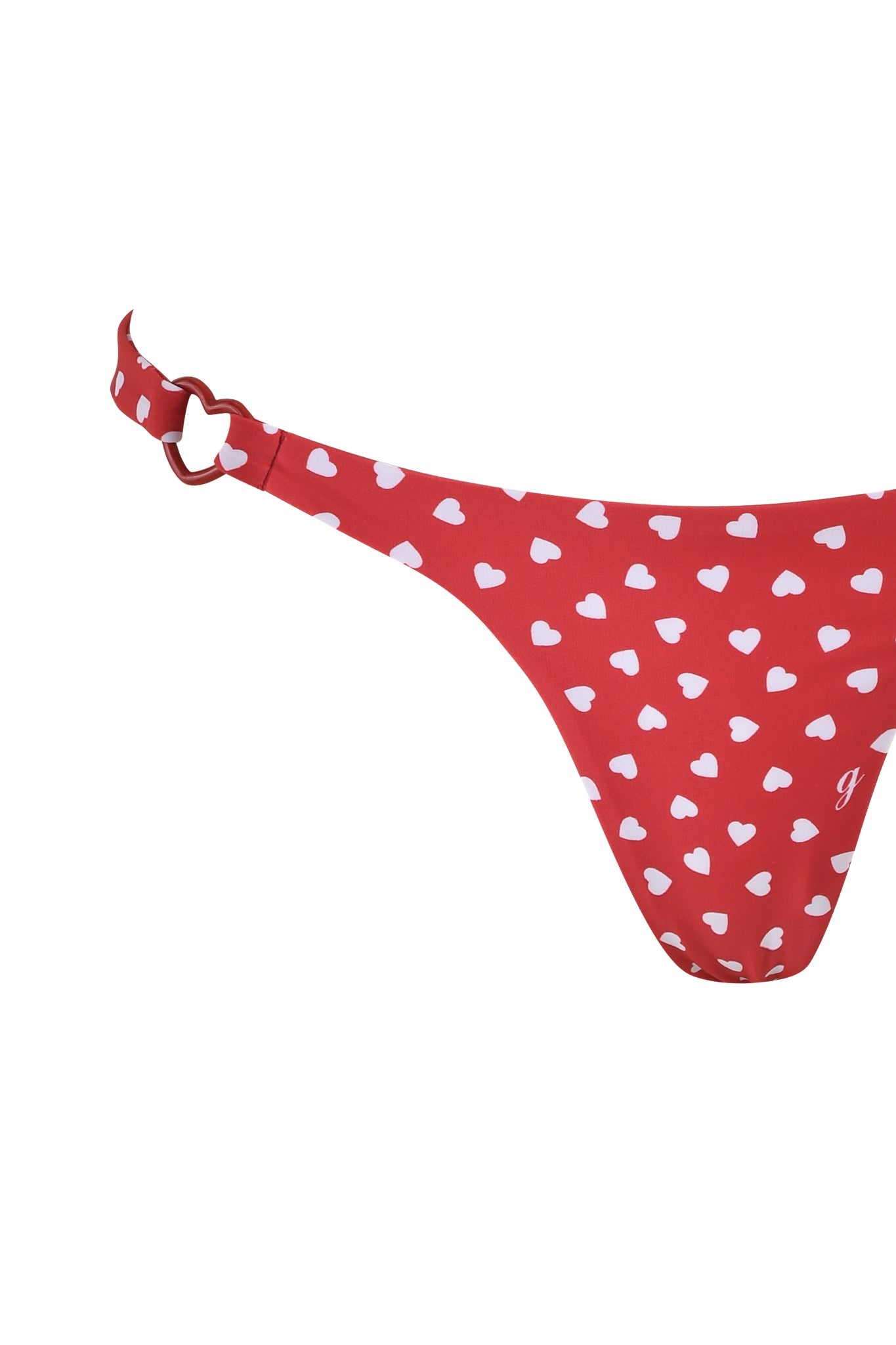 The VALENTINA BIKINI BOTTOM - RED HEARTBEAT by I.AM.GIA is a red low-rise thong with a GIA heart print, featuring white hearts and adorned with a side strap heart-shaped ring. The fabric is smooth and stretchy.