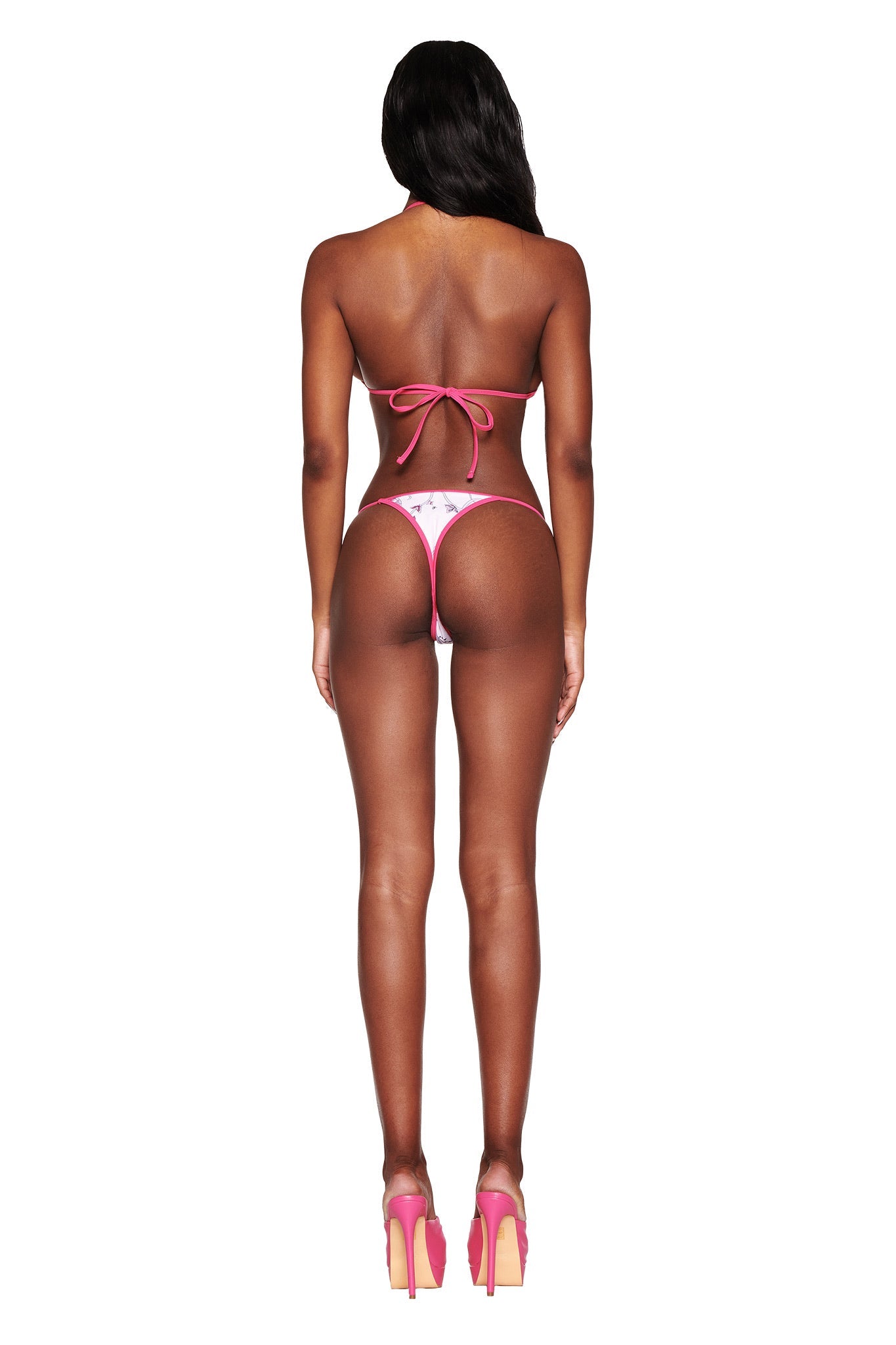 A person with long dark hair wears the I.AM.GIA CORDELIA 2.0 Bikini Top in pink butterfly ribbon and high heels, standing against a plain background. The bikini top complements the star-patterned bottoms, adding an enchanting touch to the ensemble.