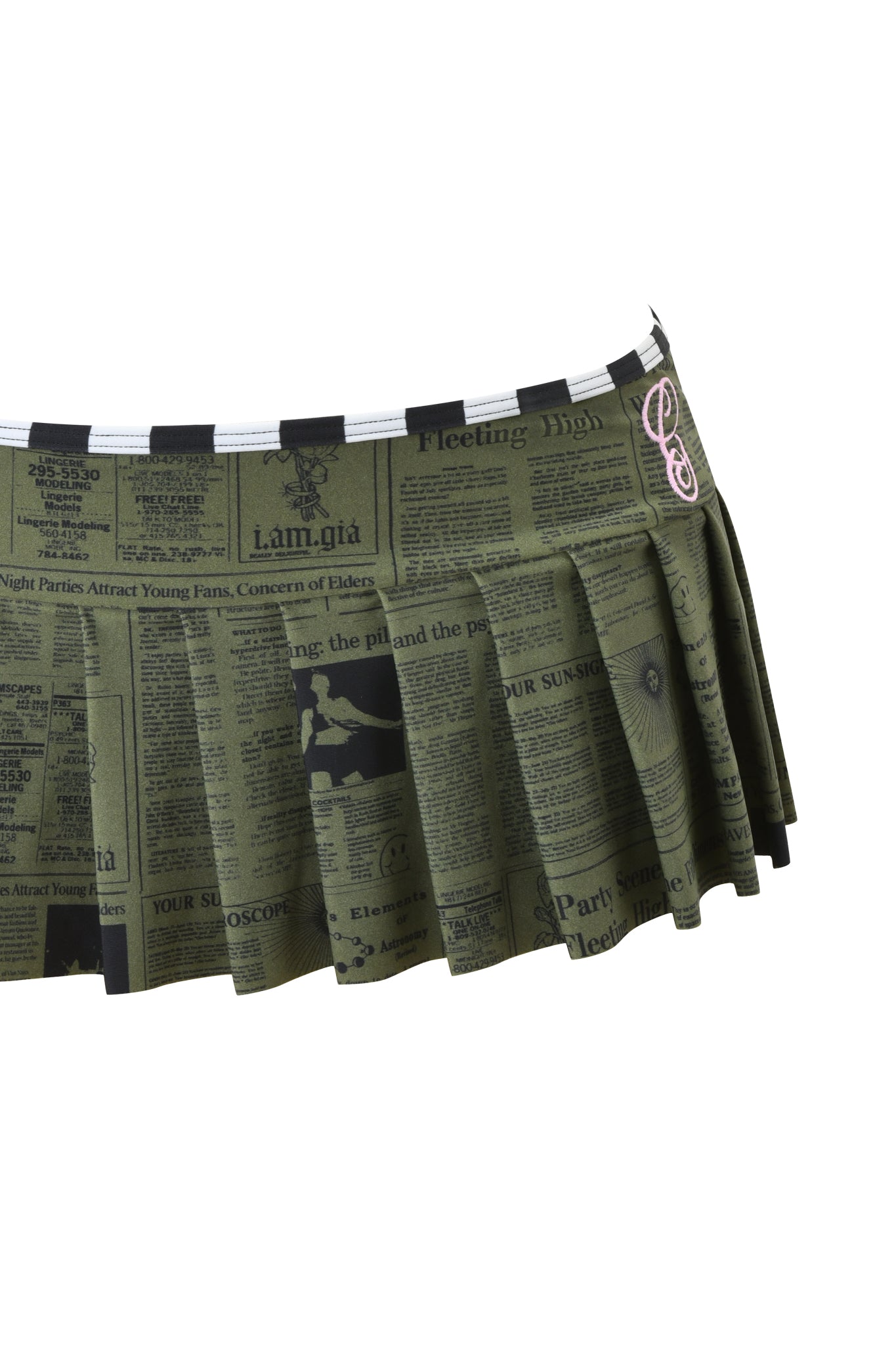 The I.AM.GIA AURETTE MICRO BIKINI SKIRT - LEFT ON READ is a green pleated mini skirt with a black newspaper print and a small pink treble clef symbol near the waistband.