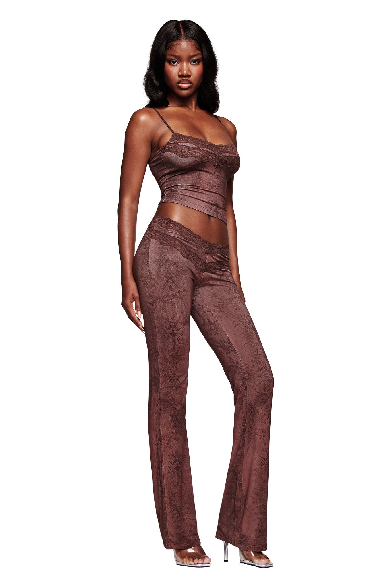 A woman wears I.AM.GIA’s BEAU PANT - BROWN, a lace-printed low-rise flared lounge pant set with matching brown camisole and sheer details, styled with high-heeled sandals against a white background.